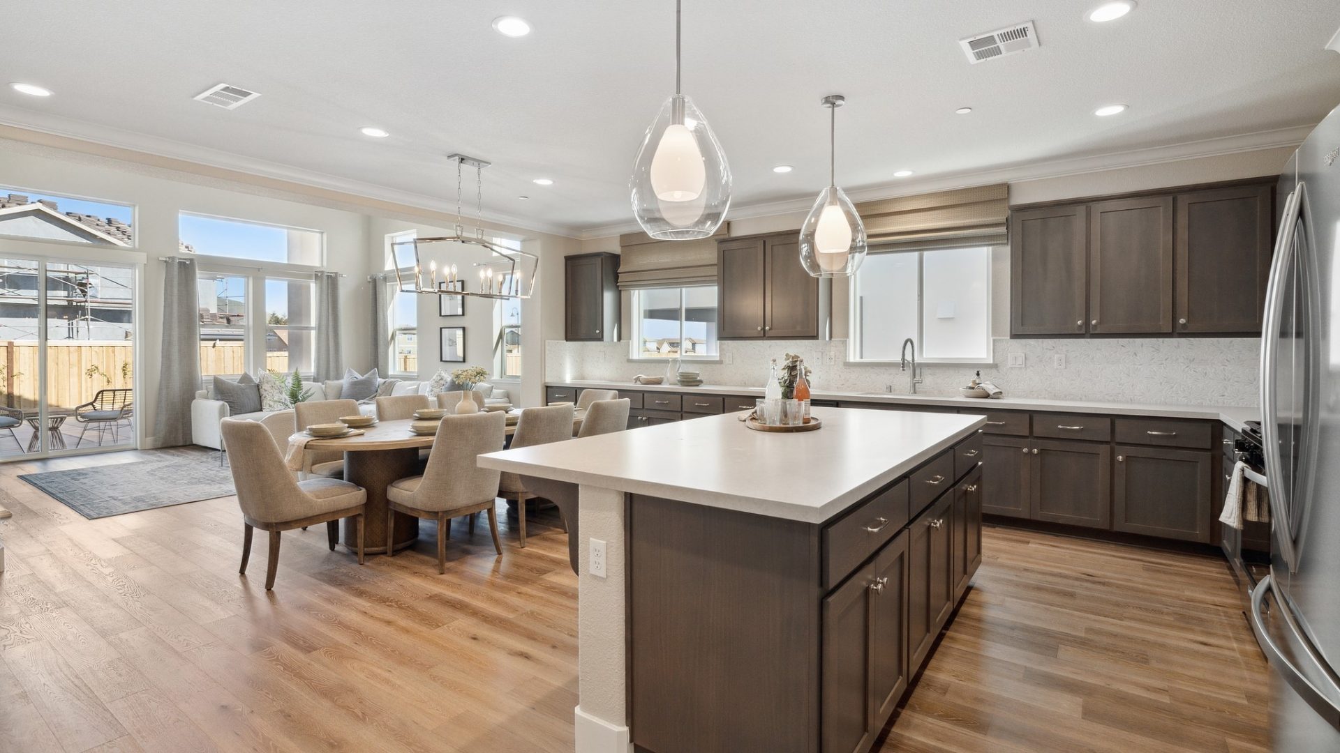Open kitchen and living room layout with hardwood floors, dark beech wood cabinets, white quartz countertops, 2 pendants over kitchen island, stainless steel appliances, and 9 foot ceilings with canned lighting.