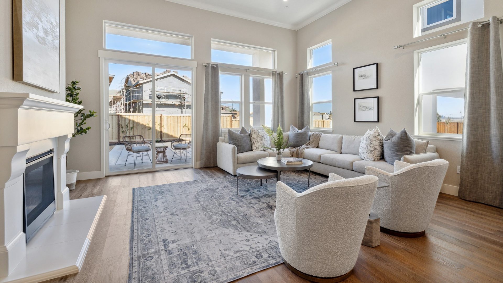 Large open living room with fireplace, hardwood floors, tall windows with tons of natural light, accent rug, barrel chairs, and couch.