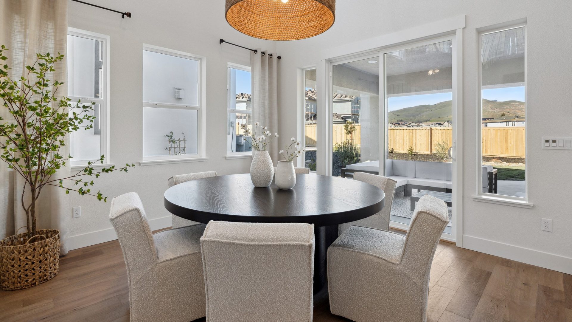 Kitchen table nook  with four chairs, hardwood floors, tall ceilings and large pendant chandelier, looking out 4 large widows and large glass sliding door.
