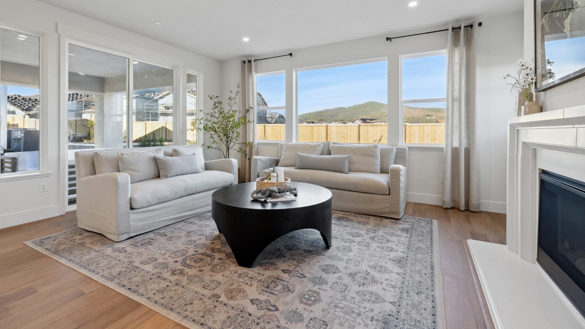 Large open living room with hardwood floors, 2 couches, accent rug, coffee table, 9 foot ceiling with canned lights, 5 large windows looking out to the backyard with large sledding glass doors.