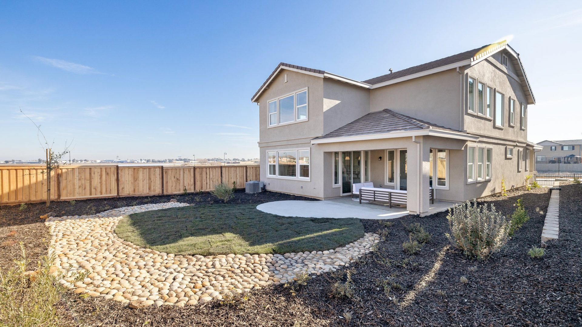 Exterior backyard 2-story home elevation painted in beige tones, with covered porch and grass landscaping.