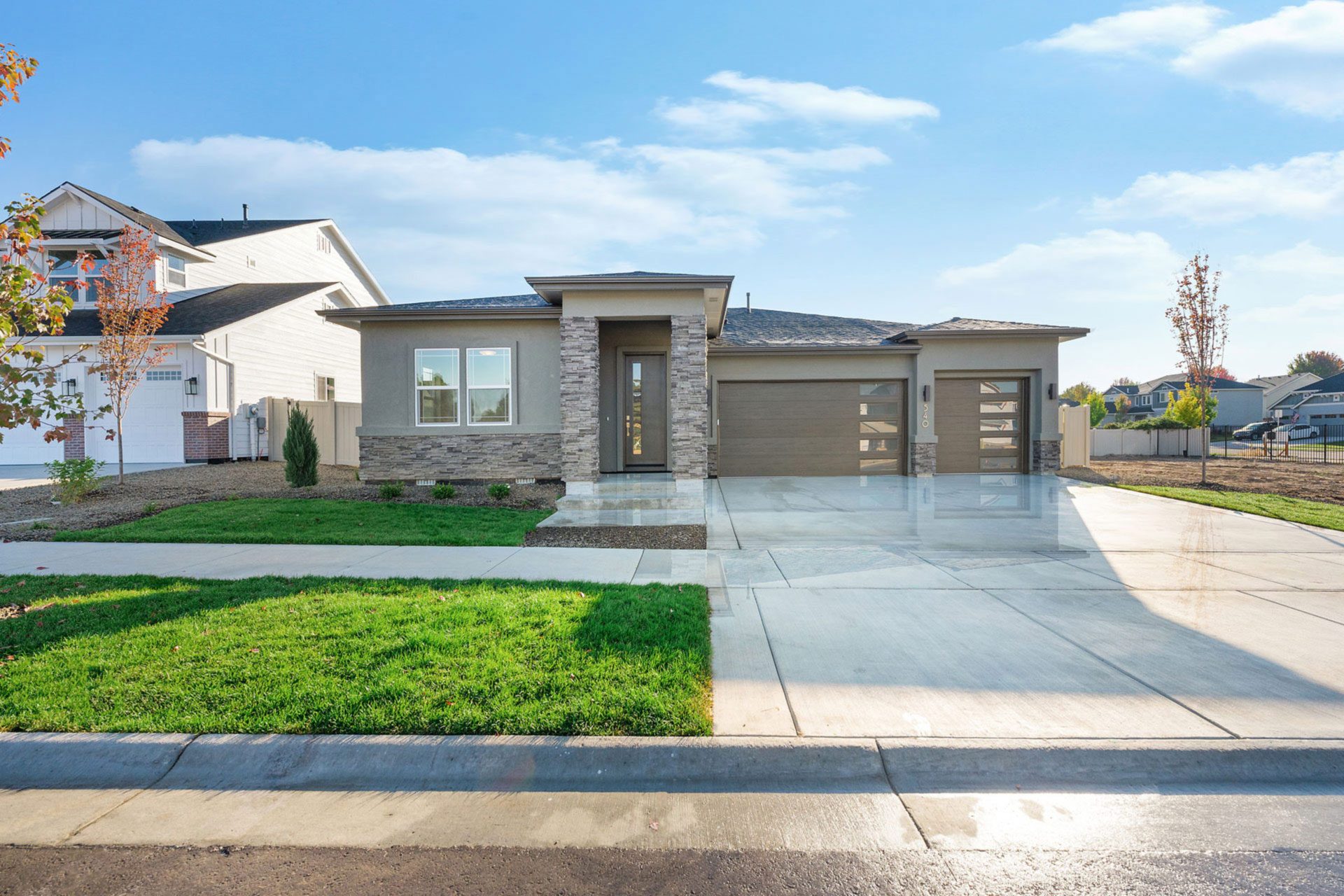 External elevation of craftsman style 2-story home with stonework facade and painted in dark grey and brown tones with covered porch and grass landscaping.