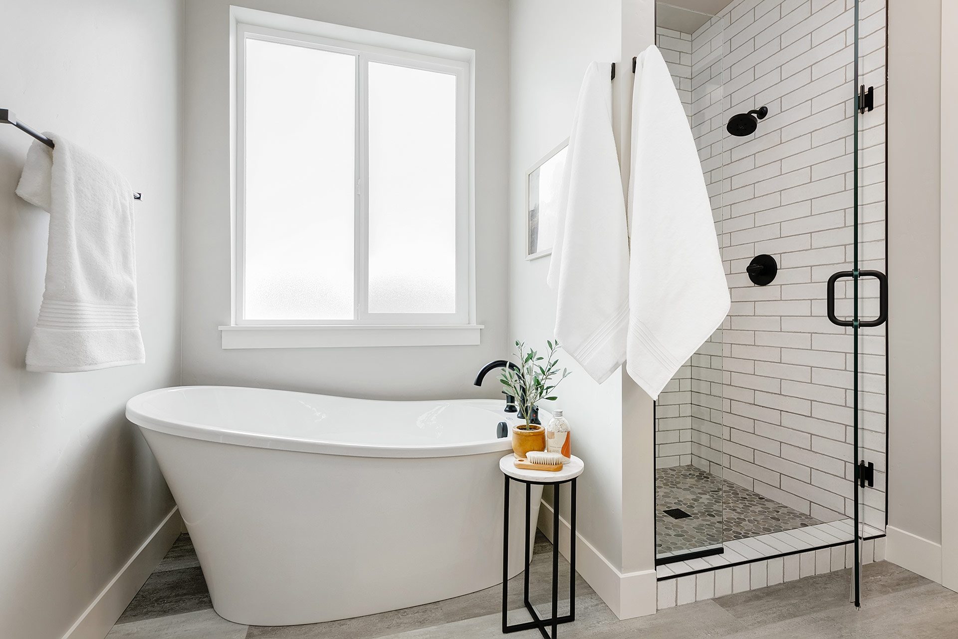 Tiled bathroom with glazed window over a soaking tub next to a tiled walk-in shower with black fixtures and glass doors.