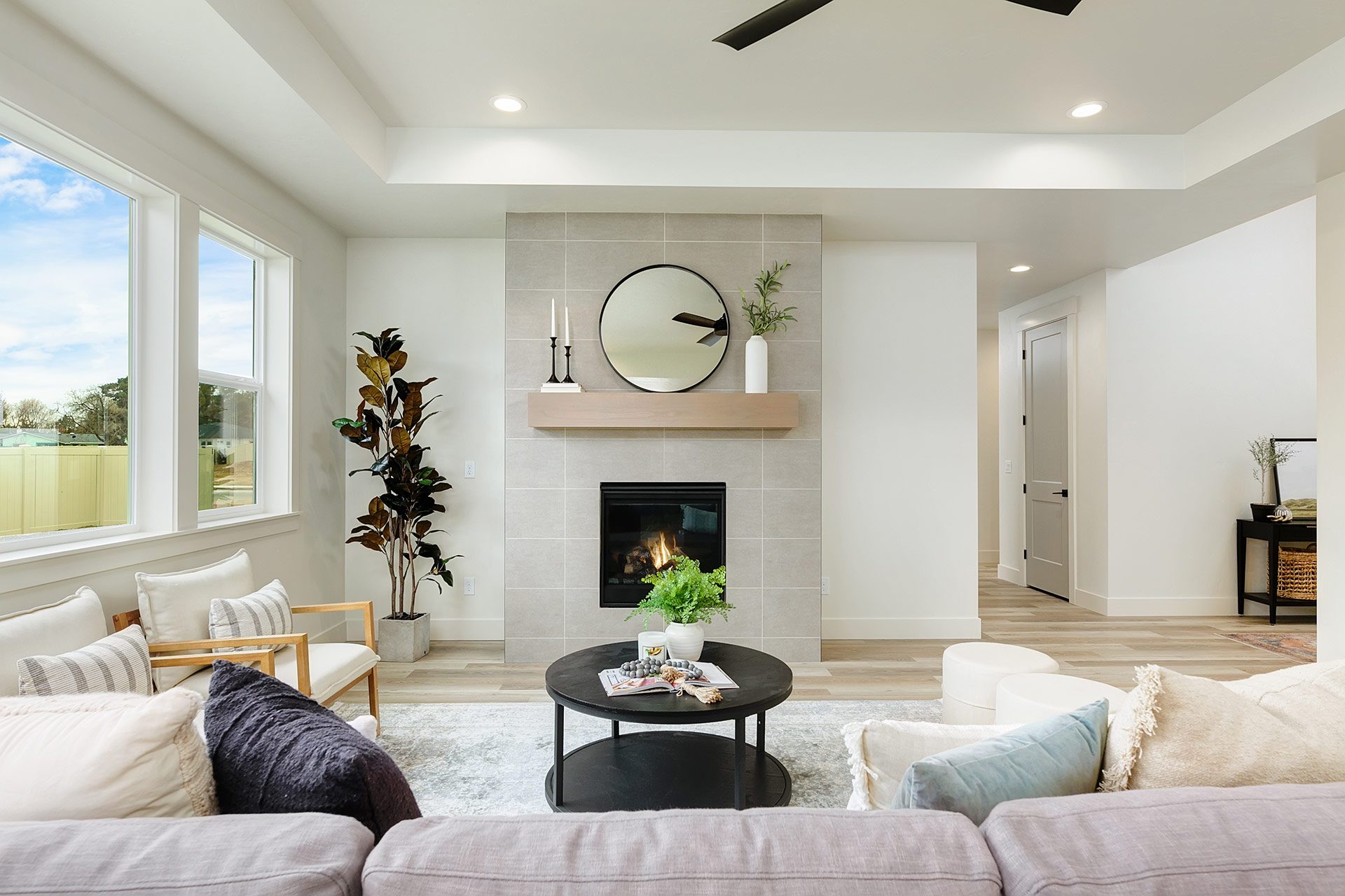 Large living room with designer furniture, hardwood floors, 3 large windows, tall mantel with electric fireplace, 9 foot recessed ceiling with canned lights and ceiling fan.