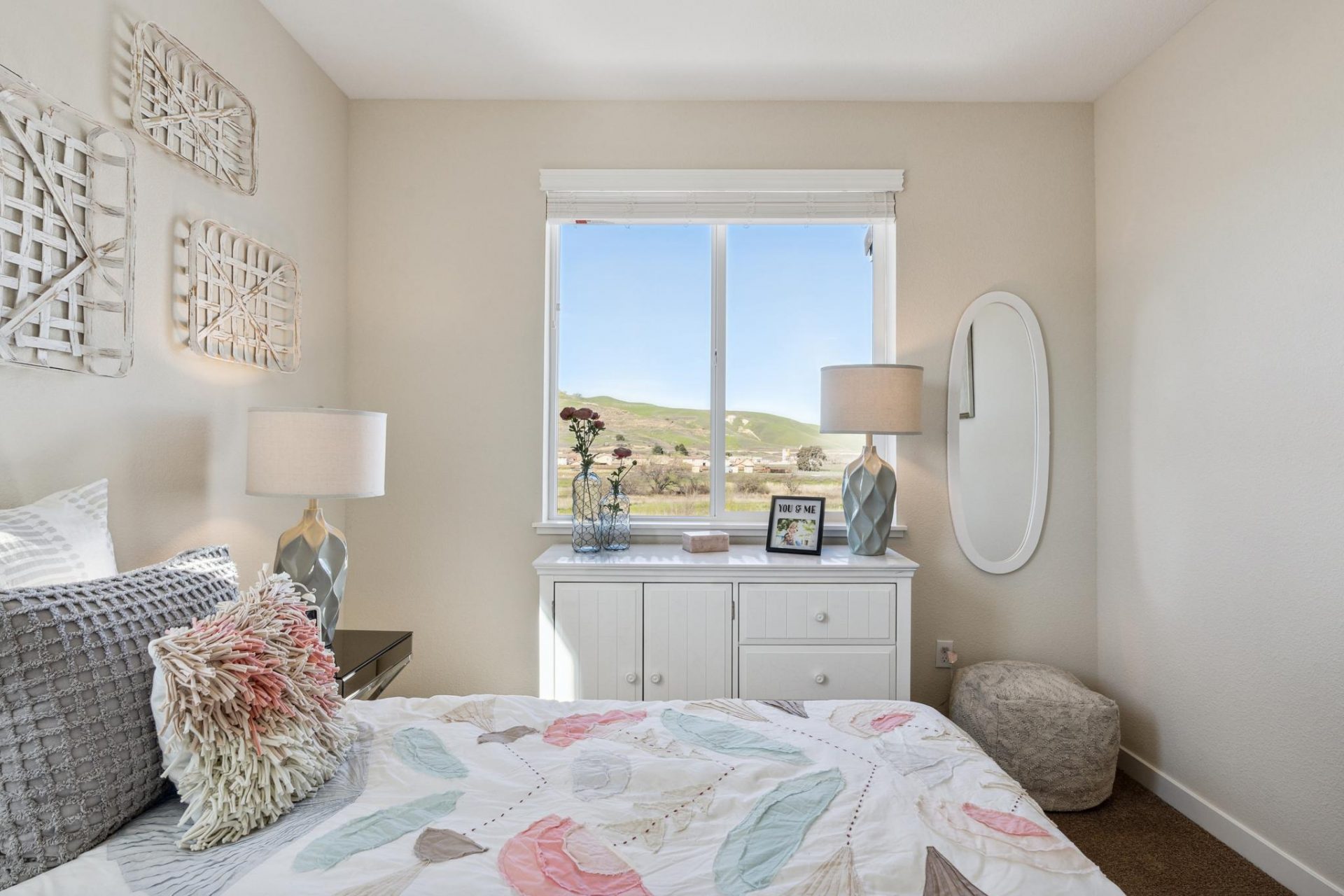 Carpeted bedroom with large window, white dresser, art hung above the bed with designer linens.