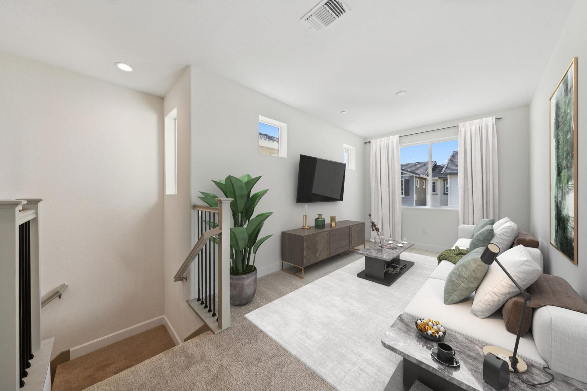 A loft area with carpeting, virtually staged with an area rug, a couch with pillows, a brown wood toned tv stand, a mounted tv, a window with drapery, and stairs leading downwards.