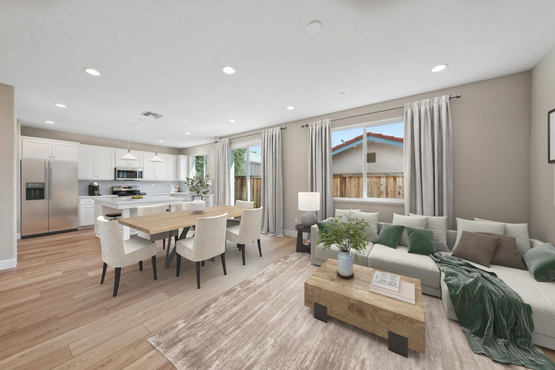 Photo of family, dining and kitchen area, virtually staged with a sectional couch with brown and green pillows and a green throw blanket, a square wooden coffee table in the family room. In the dining area a light colored wooden rectangular table with 6 c