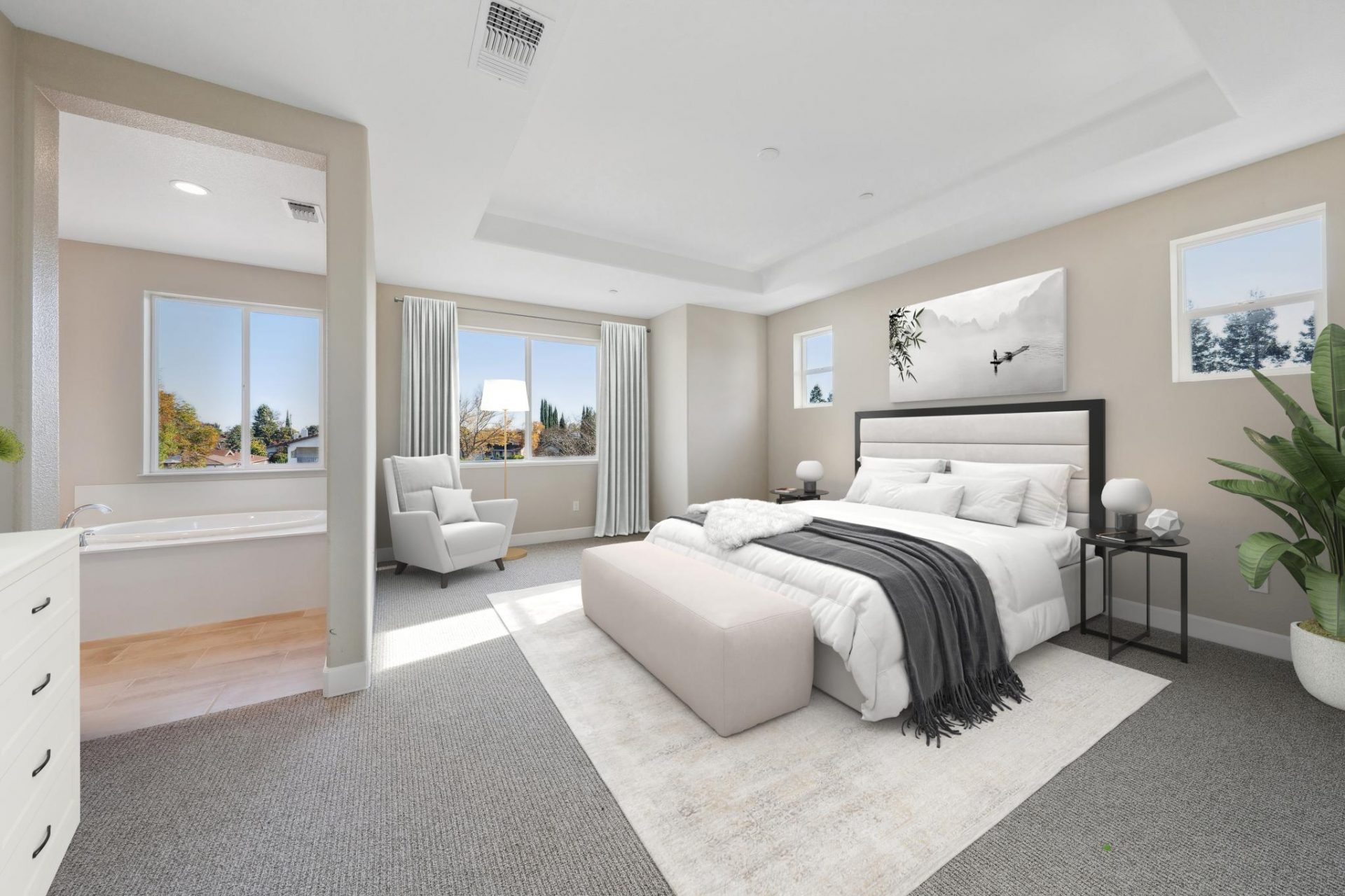 Photo of a bedroom with gray carpet, and virtually staged with a bedroom set with headboard and circular nightstands, light colored bedding, an ottoman at the foot of the bed, a potted plant in the corner and the wall the headboard is on has two windows a