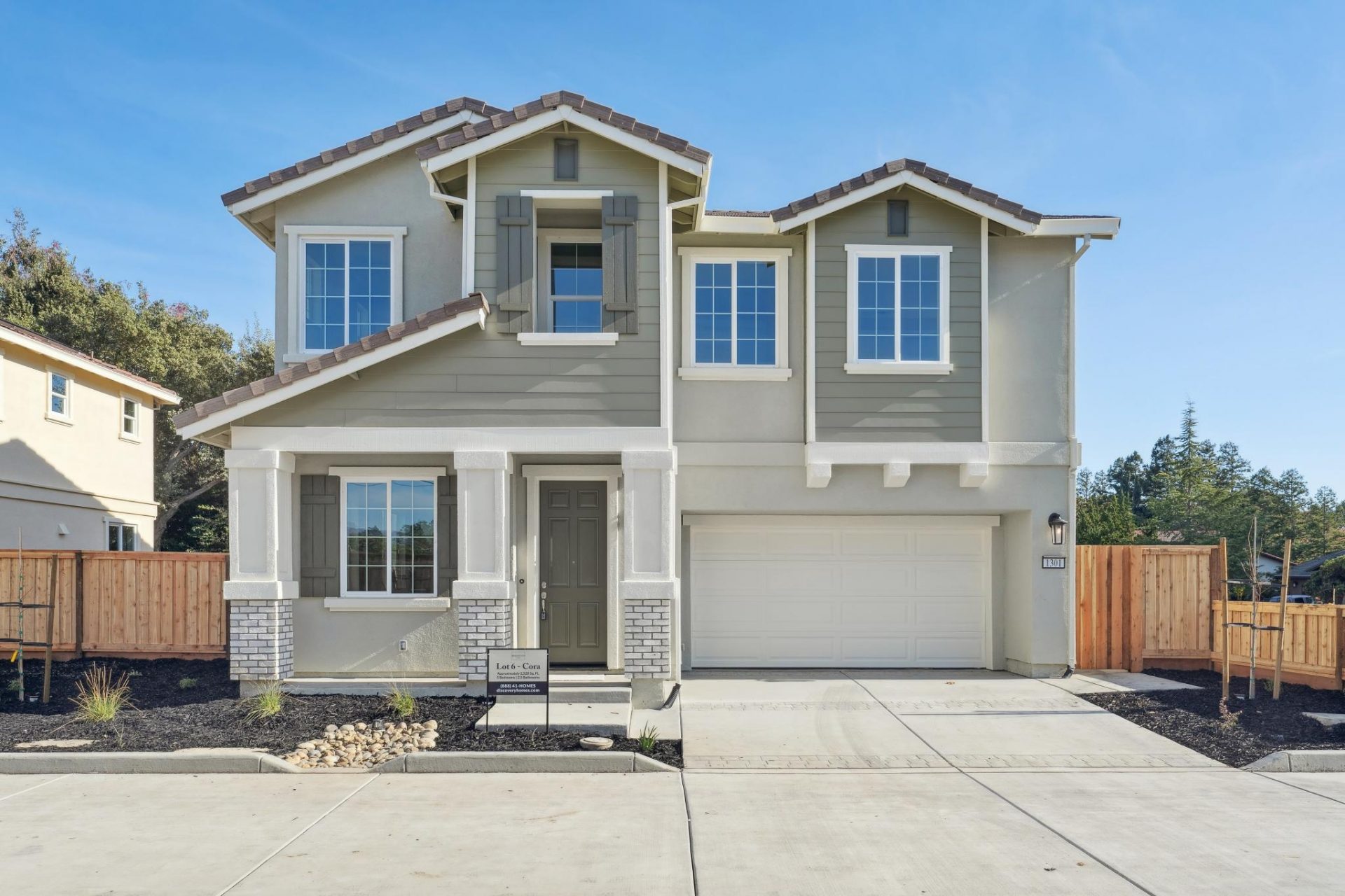 A straight view of the exterior of a modern two story home, with tile roofing, stucco and wood accents, with a three tone color scheme, light colored garage door, three pillars at the entry with stone accents.