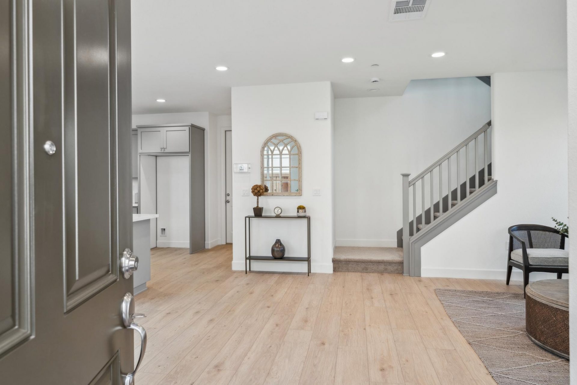 As you enter a doorway, light color wood flooring, an open space with furniture light color walls and a staircase is seen.