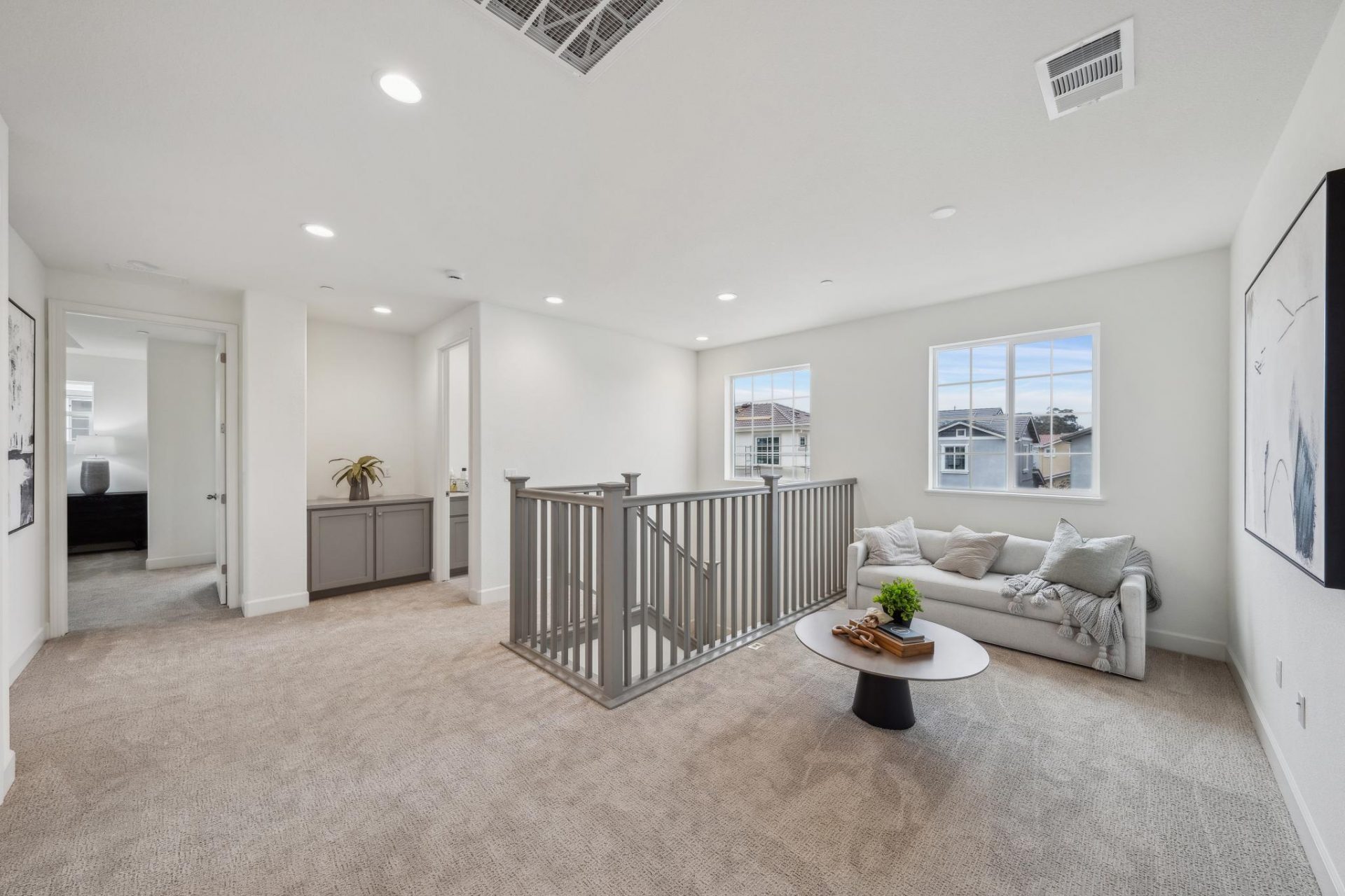A loft area with a seating area furnished with a couch, round table and miscellaneous décor. Multiple doorways leading to different rooms, top of a staircase and a gray inset storage cabinet is seen.