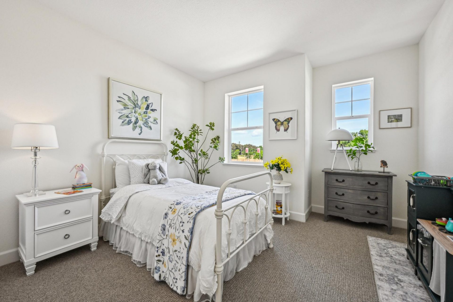 Carpeted bedroom with 2 windows, twin size bed with designer linens, 2 nights stands with lamps, and 9 foot ceilings.