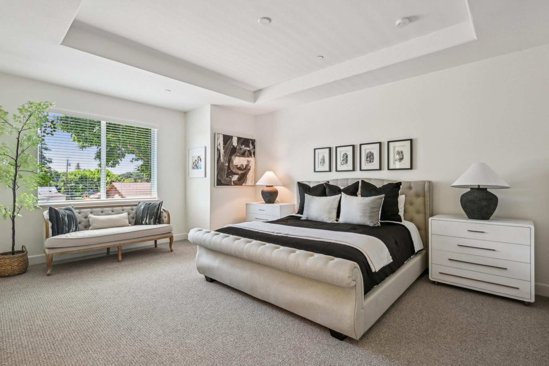 Carpeted primary bedroom suite with 9 foot recessed ceiling, canned lighting, large glass slider window, king bed with designer linens framed with 2 nightstands.
