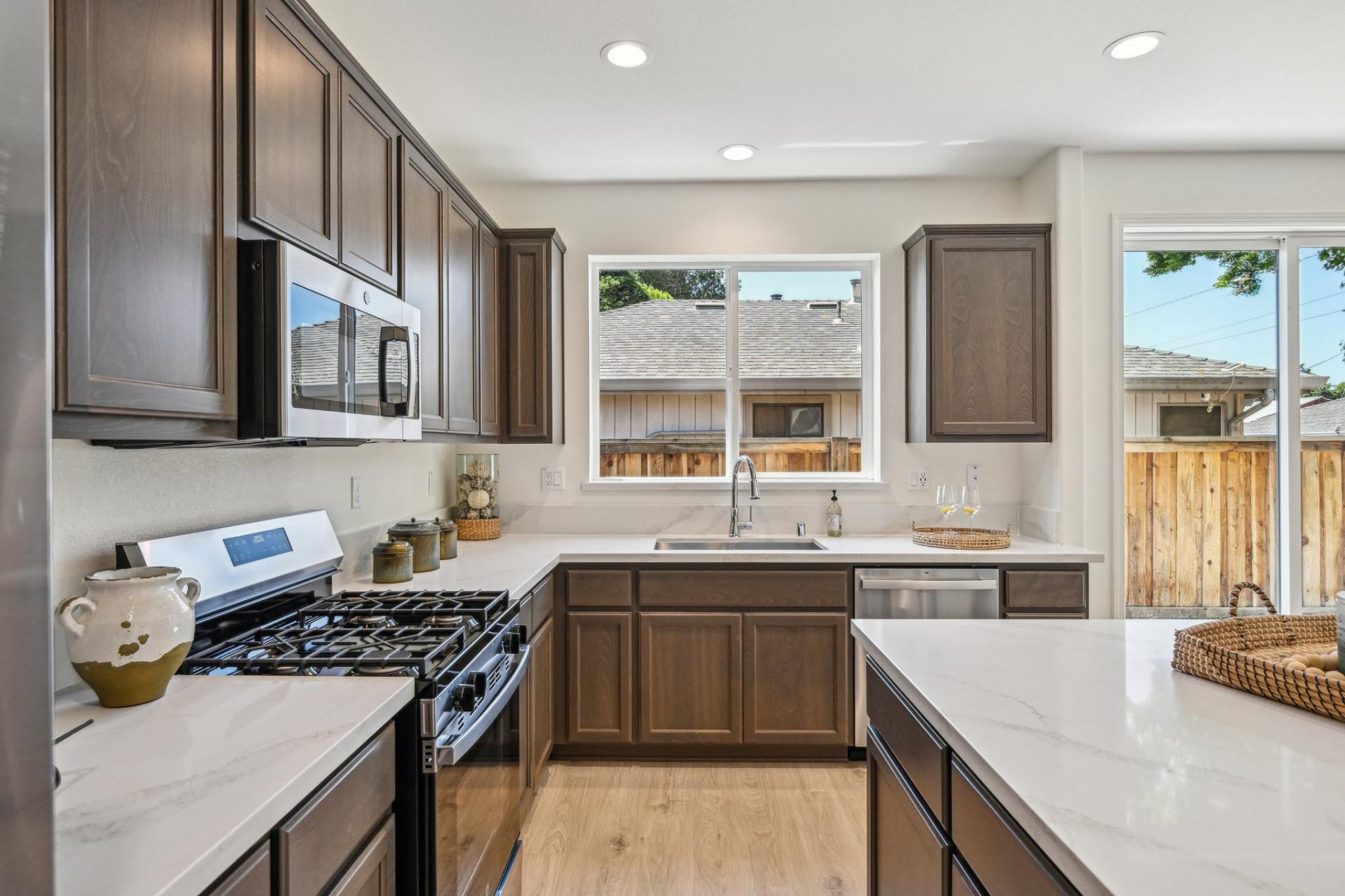 Open concept chef's kitchen with dark beech wood cabinets, stainless steel appliances, white quartz countertops and tiled backsplash, kitchen island, 9 foot ceilings with canned lighting, large window over the kitchen sink and large slider glass doors.