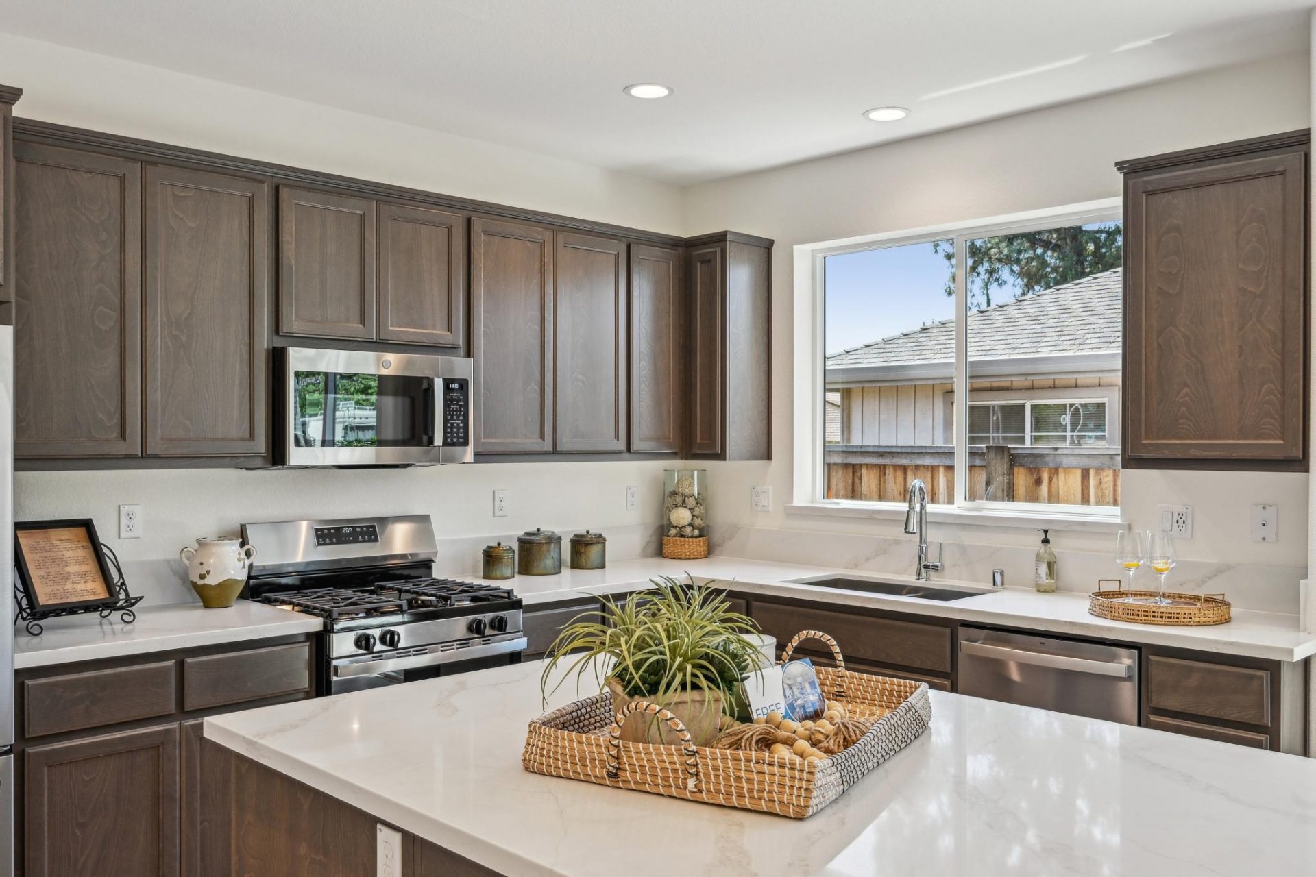 Dark beech wood kitchen cabinets with white quartz countertops, stainless steel appliances, large kitchen window over the sink, tiled backsplash, and 9 foot ceilings with canned lighting.