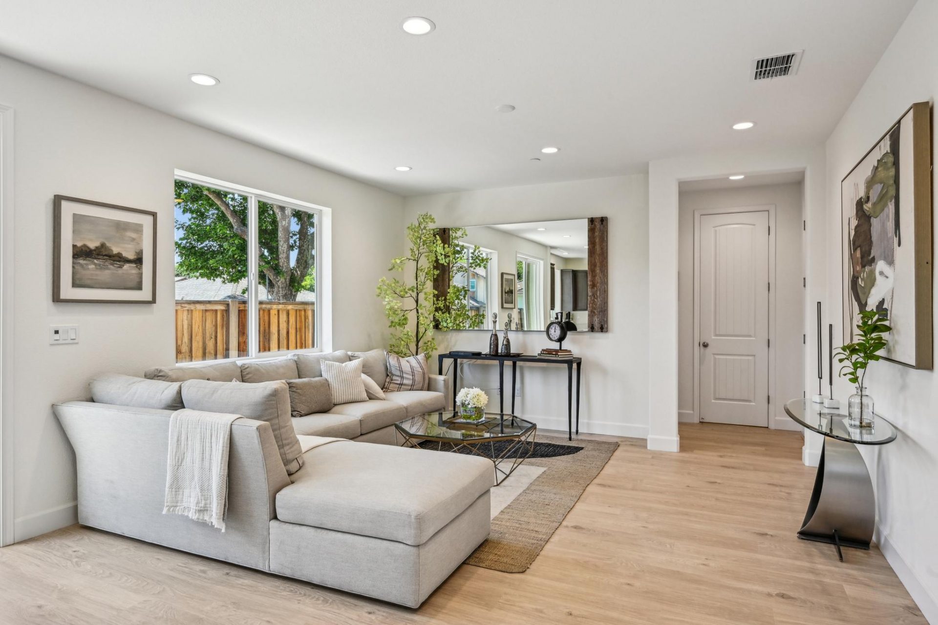 Living room with chaise couch, accent rug, large window looking out to the backyard, 9 foot ceiling with canned lights and 8 foot doorway entrance to hallway.