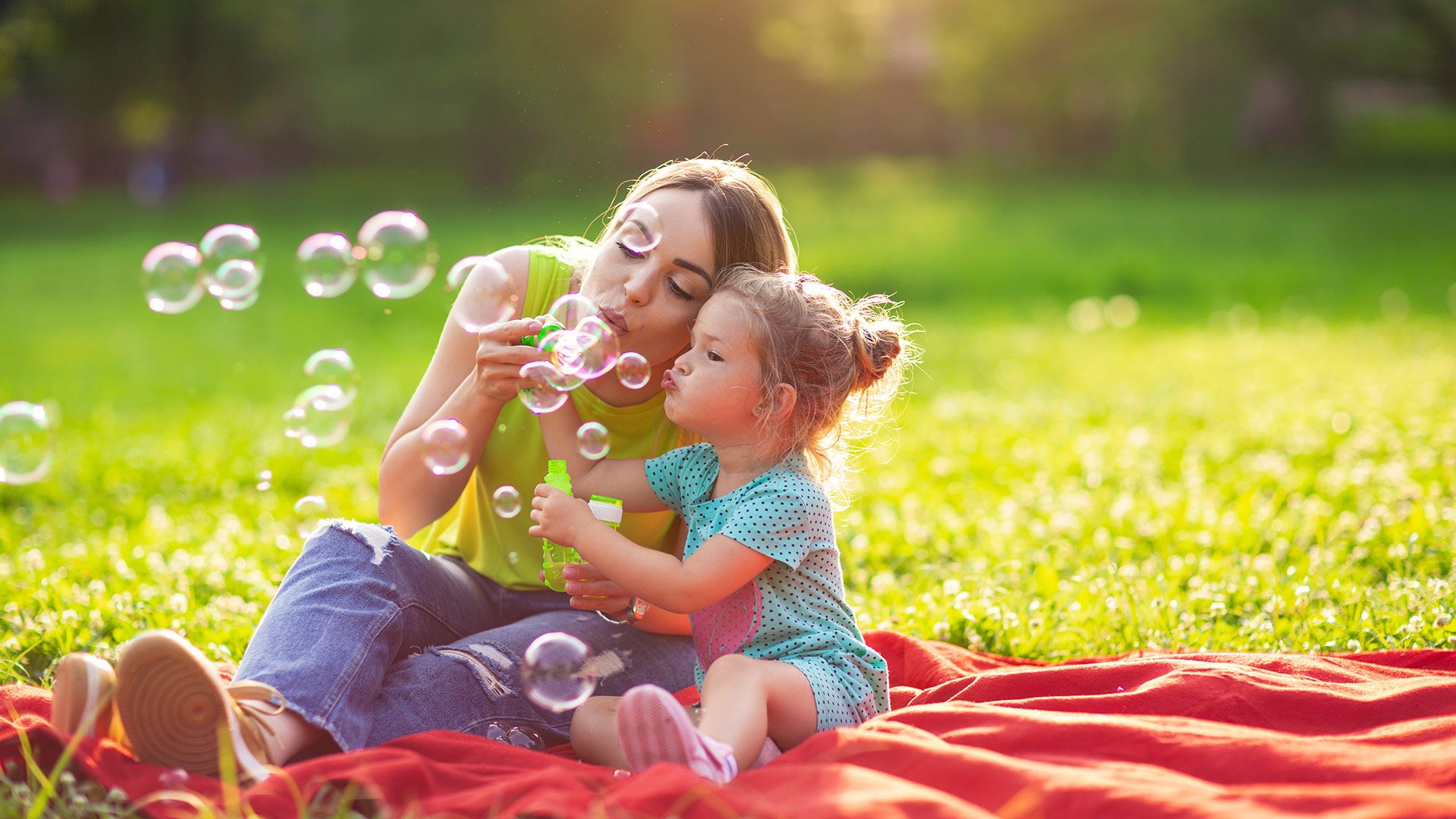 2 kids lowing bubbles on a red blanket in grass park