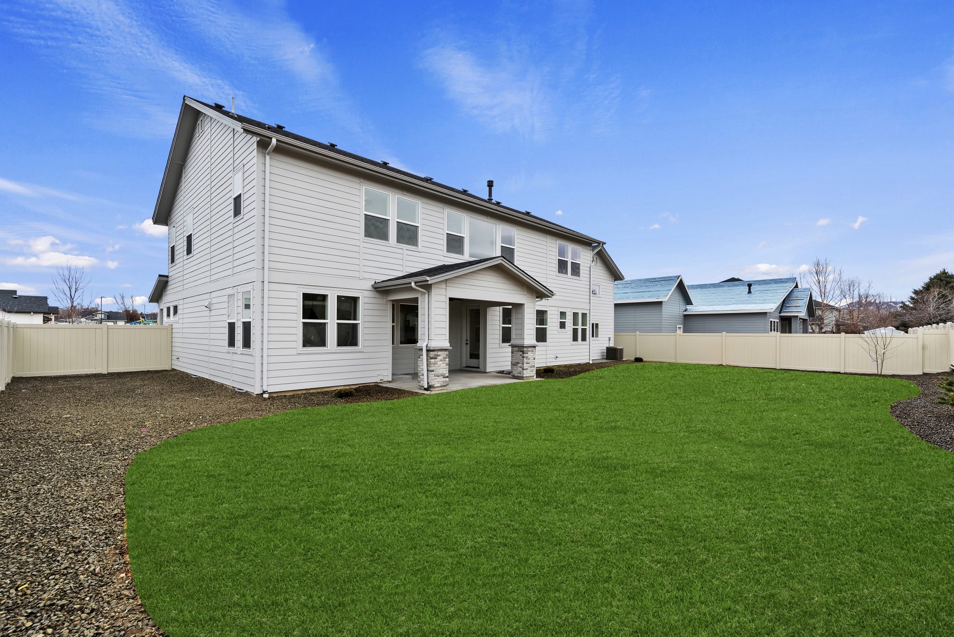 Side angle of exterior backyard elevation of craftsman style 2-story home painted in grey tones with covered porch and grass landscaping.