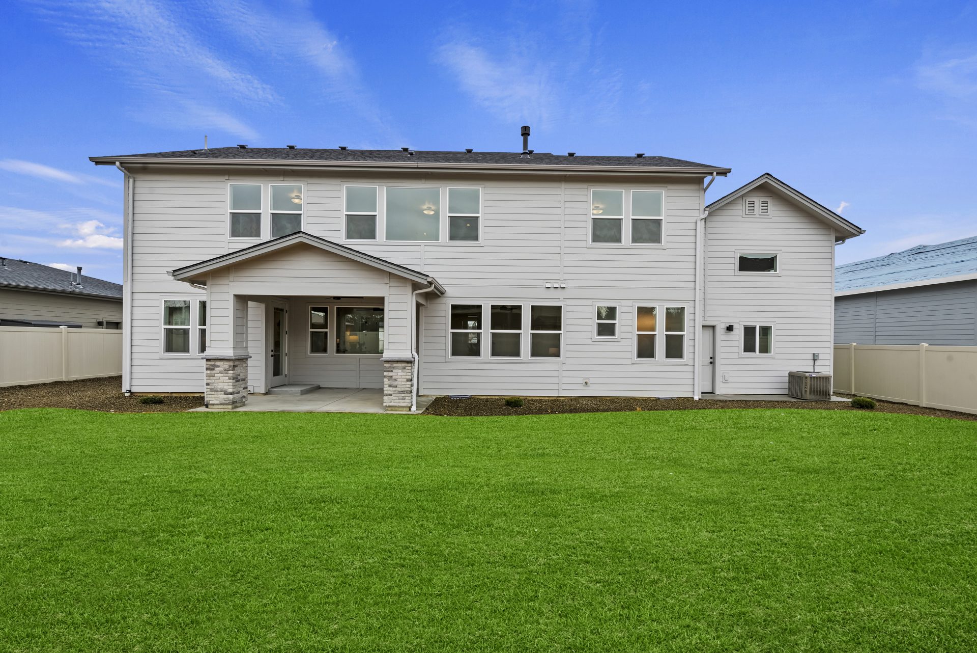 Exterior backyard elevation of craftsman style 2-story home painted in grey tones with covered porch and grass landscaping.