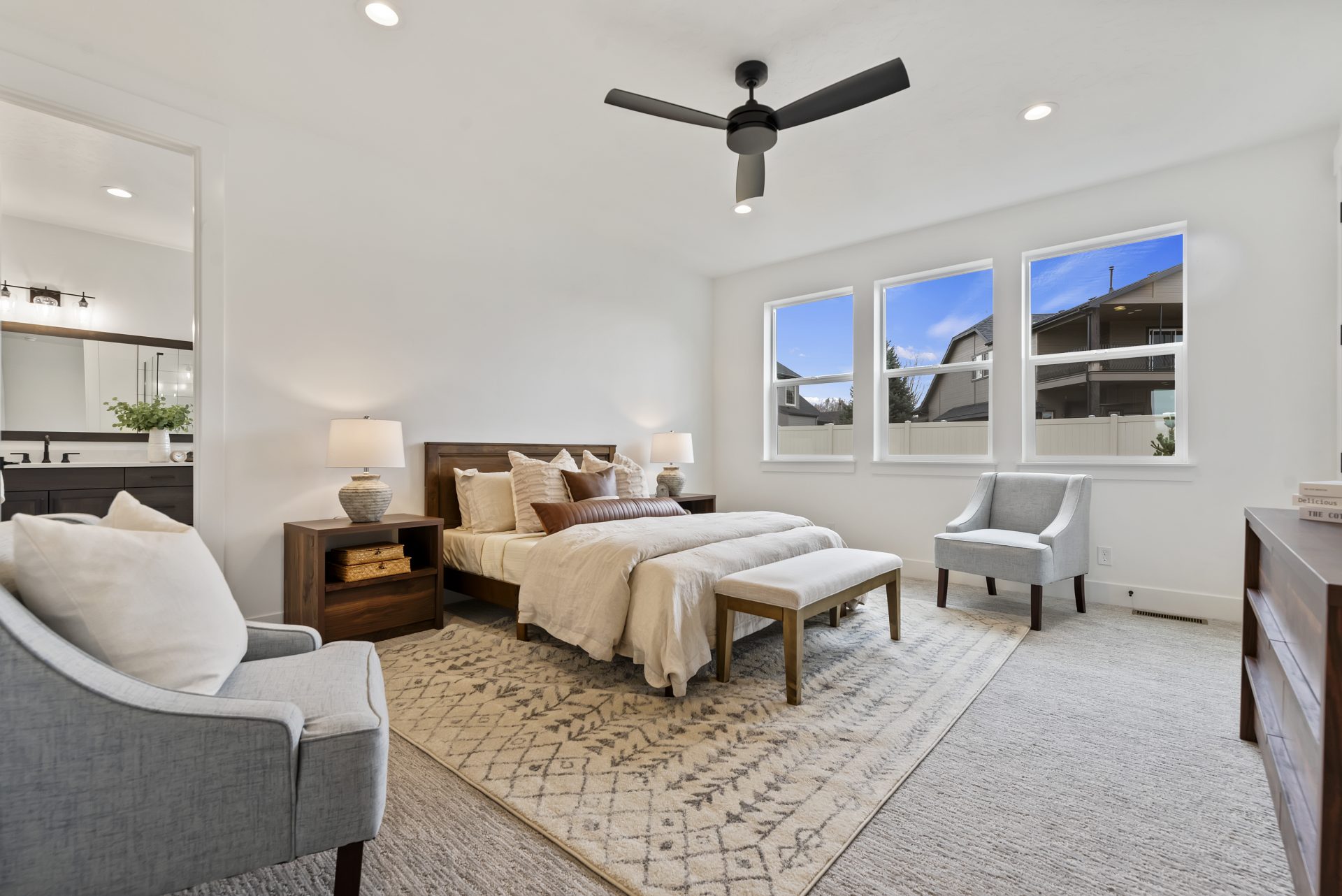 Large carpeted primary suite with king bed, 3 large windows, 9 foot ceiling and canned lights with ceiling fan, and 8 foot doorway to the primary bathroom.
