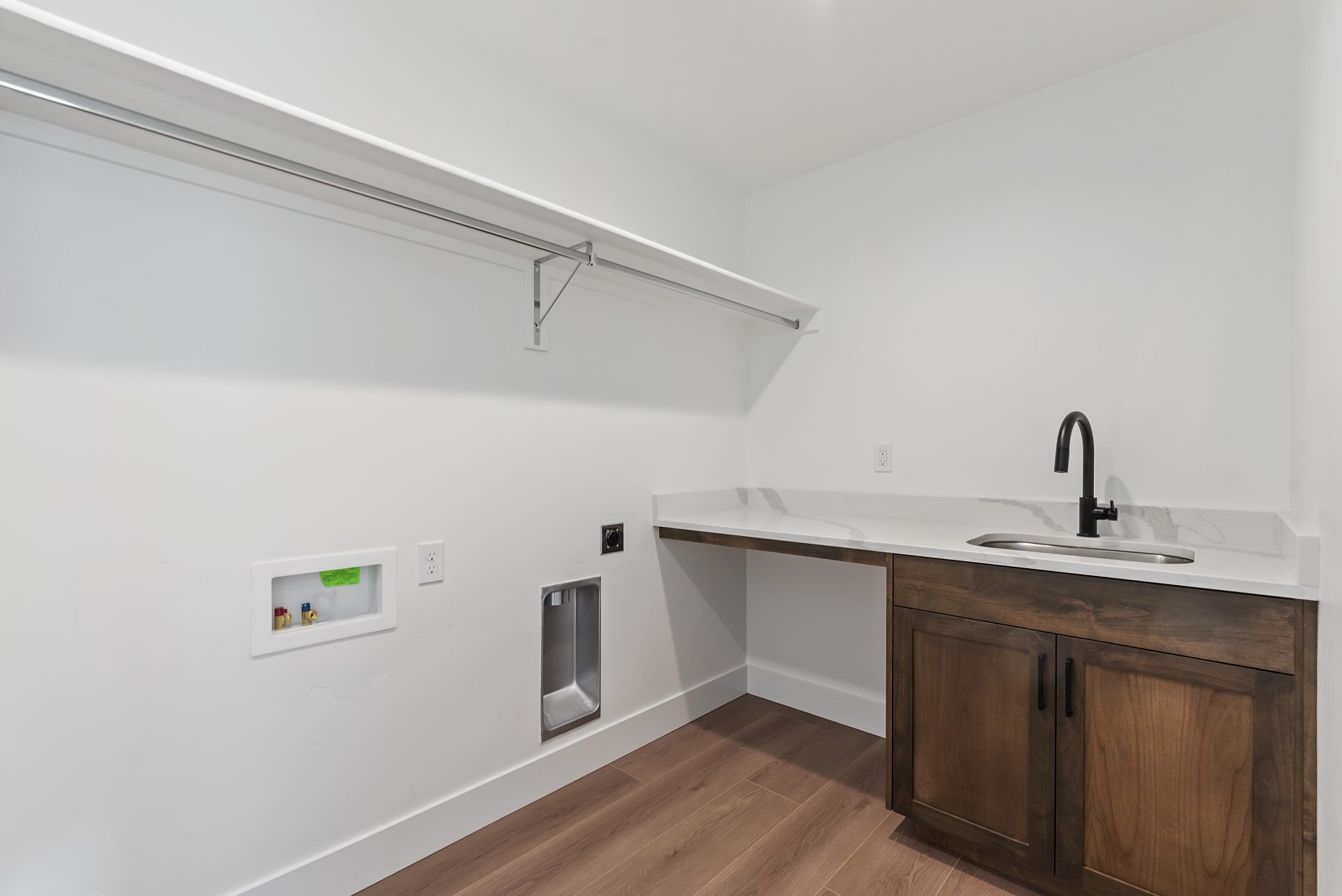 Laundry room with a long shelf running the length of the space, a single sink with a stained brown vanity, and medium brown wood flooring. No washer or dryer is present.