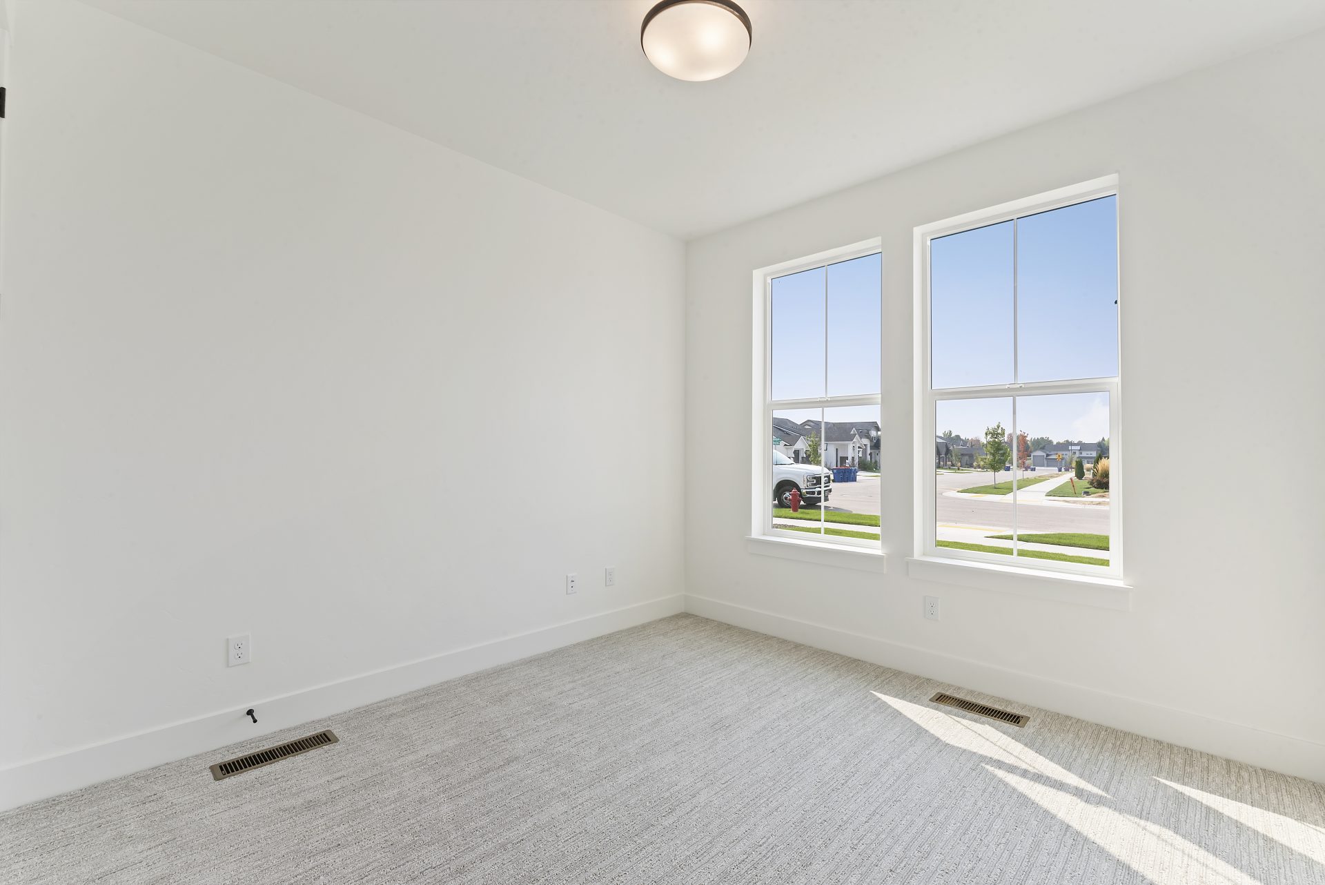 Bright bedroom featuring two equal-sized windows, each approximately 3 feet high by 2 feet wide, carpeted flooring, and a ceiling light