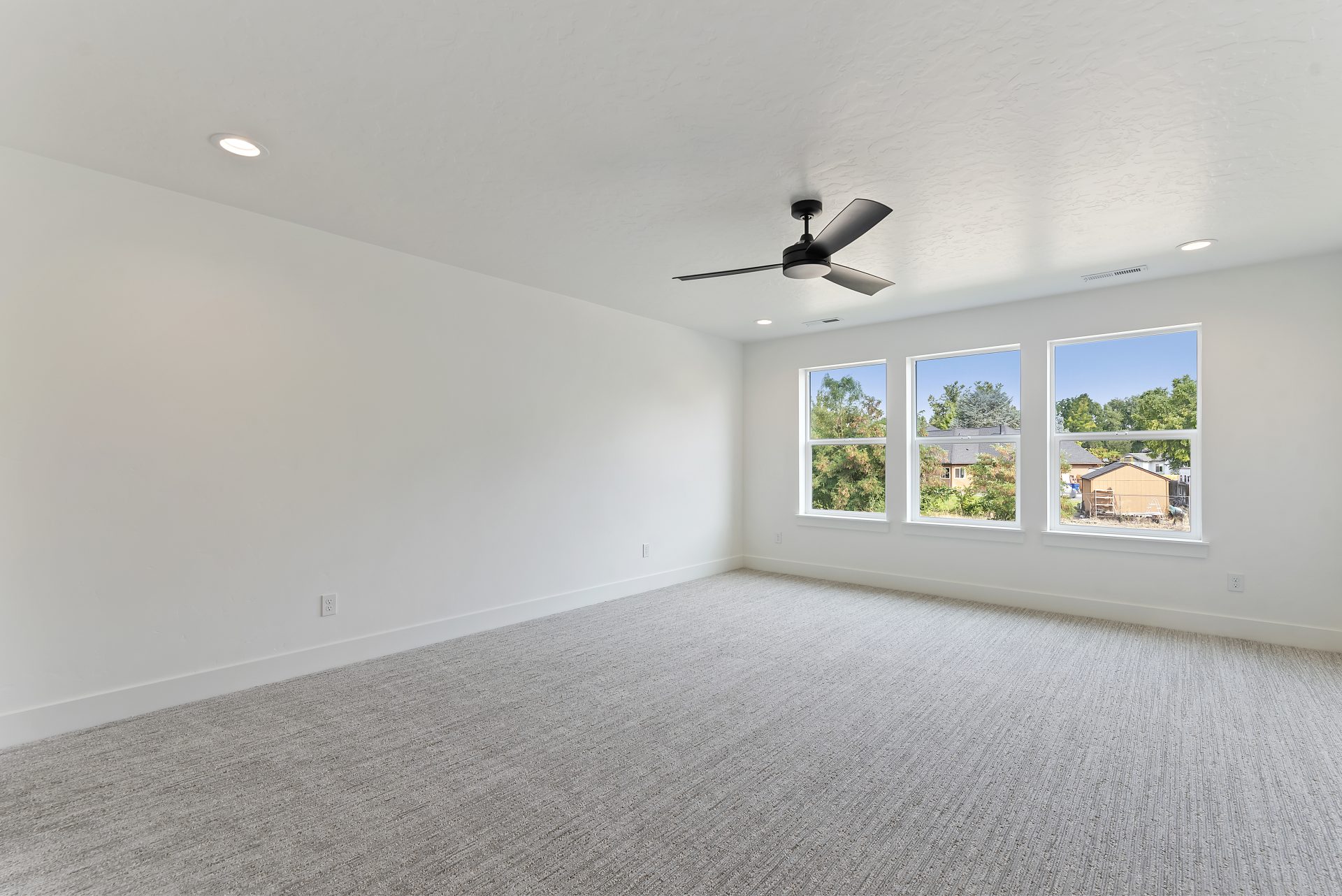 Bright bedroom featuring three equal-sized windows, each approximately 3 feet high by 2 feet wide, carpeted flooring, and a ceiling fan with light.
