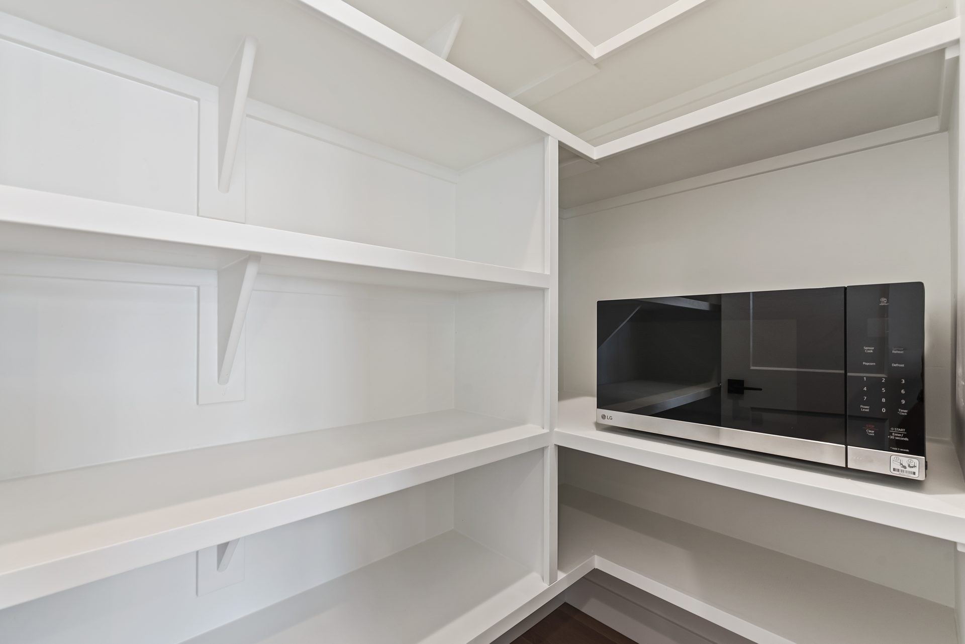 White pantry with built-in shelves and a microwave.