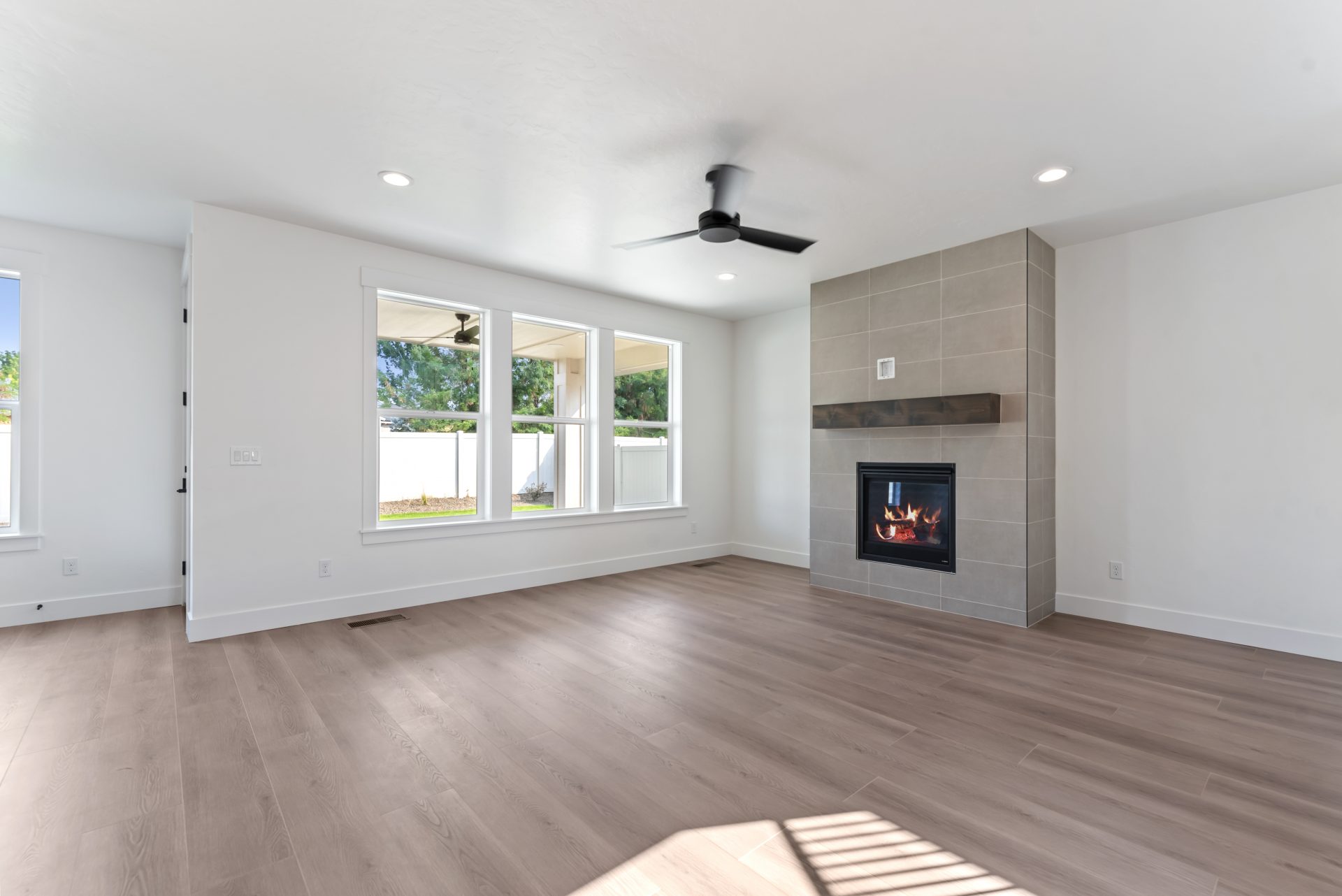 Living room viewed from another angle, featuring a fireplace with wall-to-ceiling gray tile and brown-stained mantle, and three equal-sized windows, each approximately 3 feet high by 2 feet wide