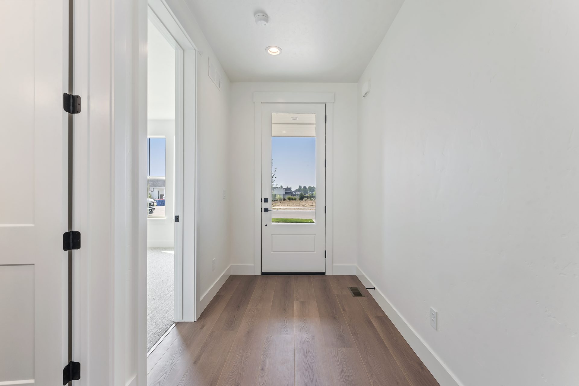 View of the entry door and hallway, featuring a door with a large window covering about half its height, one room to the left, and another doorway slightly visible.