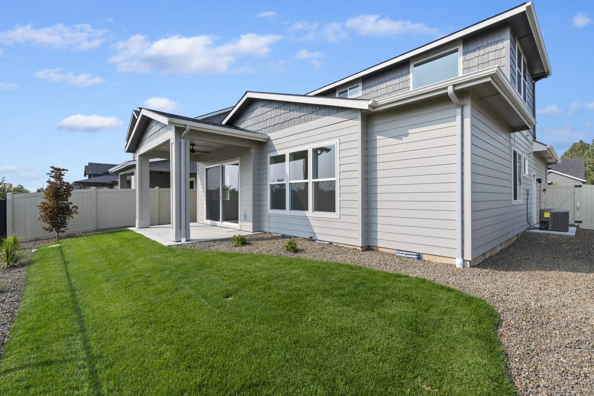 Angled view of the backyard with a modern two story home with a view of the rear and left side of the home. Landscaped backyard with plants , green grass and a small tree.