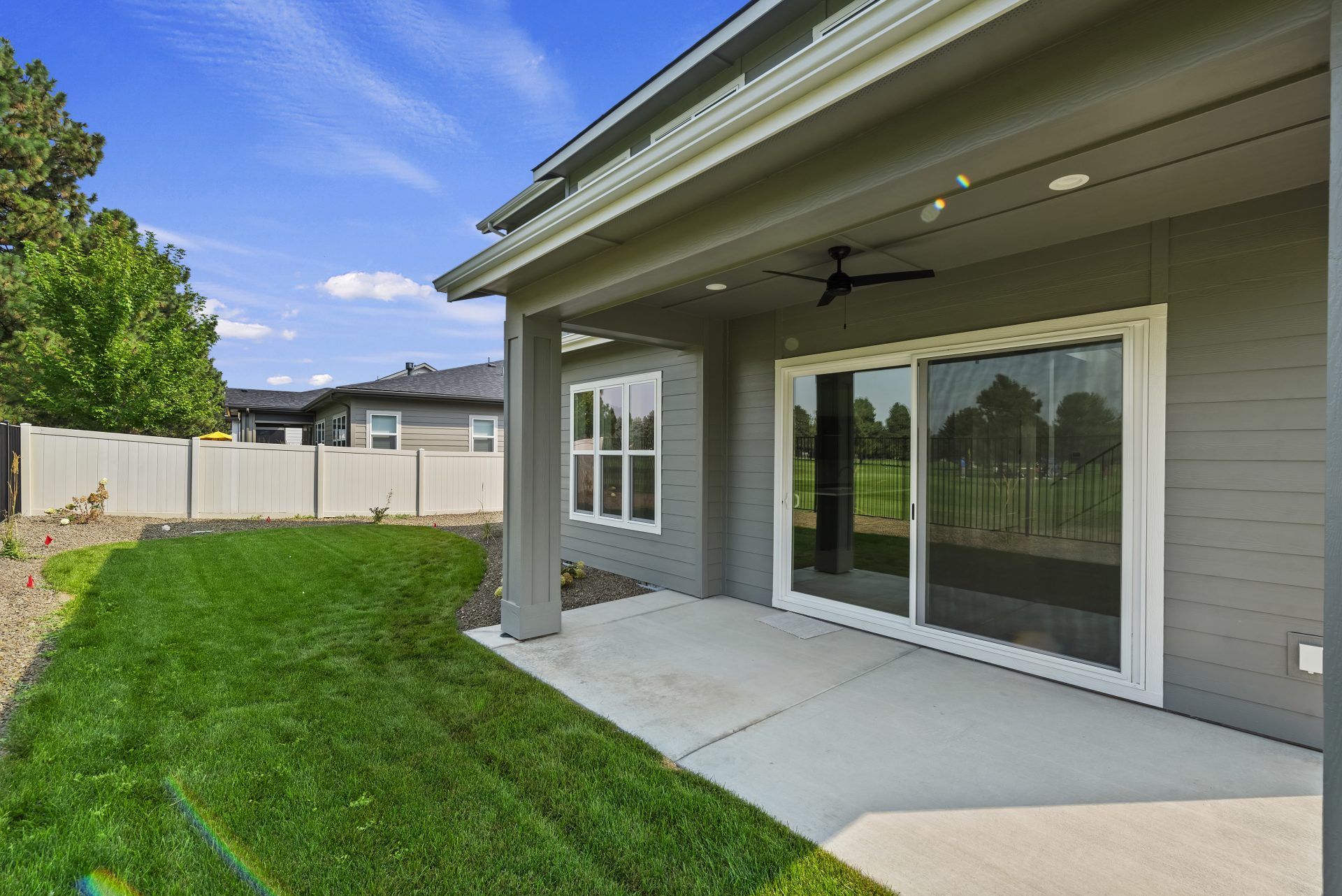 The rear of a home with gray siding and a sliding glass door with white trim, a window with 6 panels and a covered concrete porch area with an overhead ceiling fan.