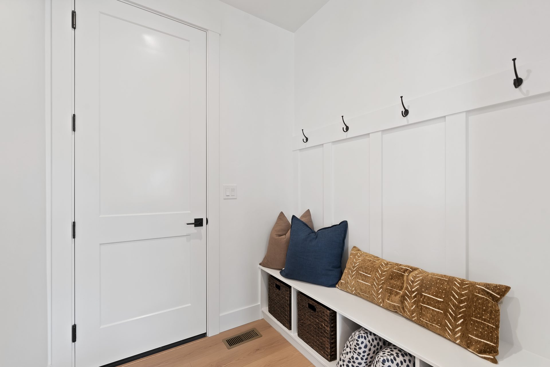 A mud room with a bench, wall paneling and hanging hooks.