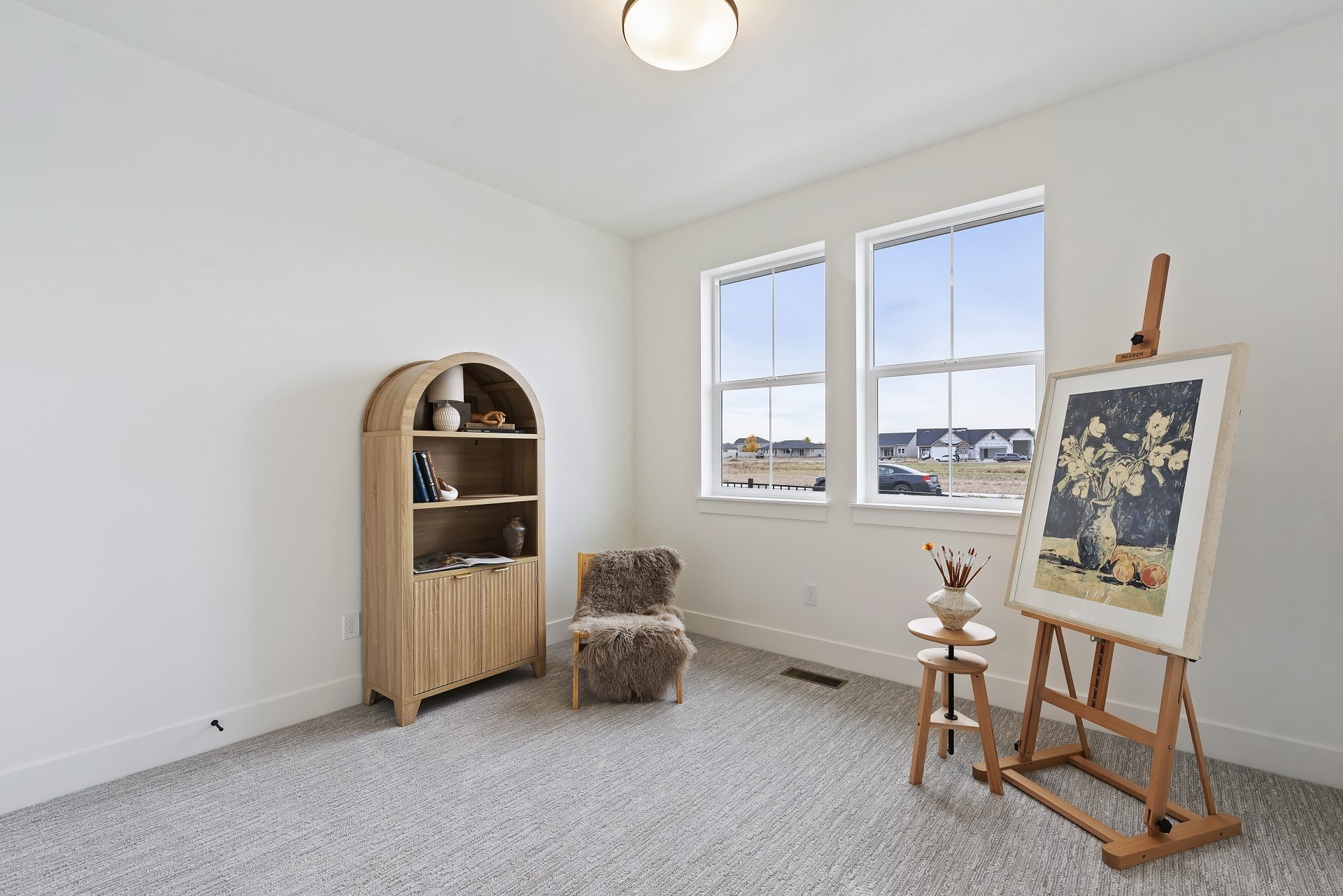 A bedroom with light color walls, gray carpeting two windows, and light staging.