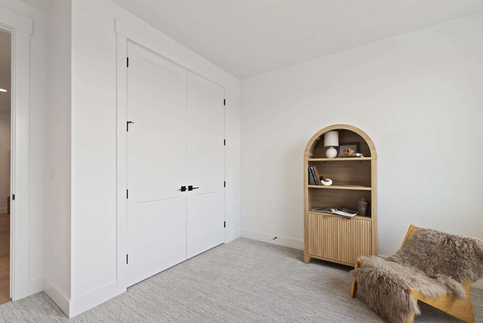 A bedroom with light color walls double door closet, gray carpeting and light staging.