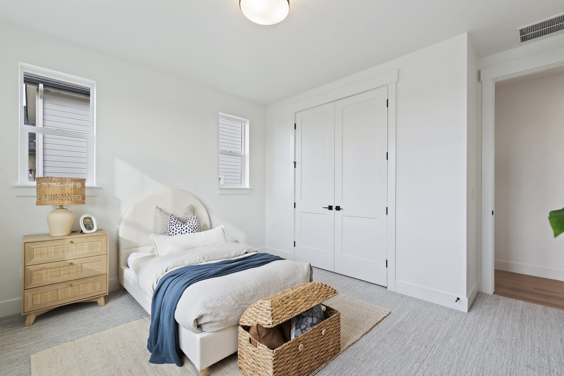 A bedroom staged with a twin bed and furniture items, gray carpet light color walls,  and a light fixture in the ceiling.