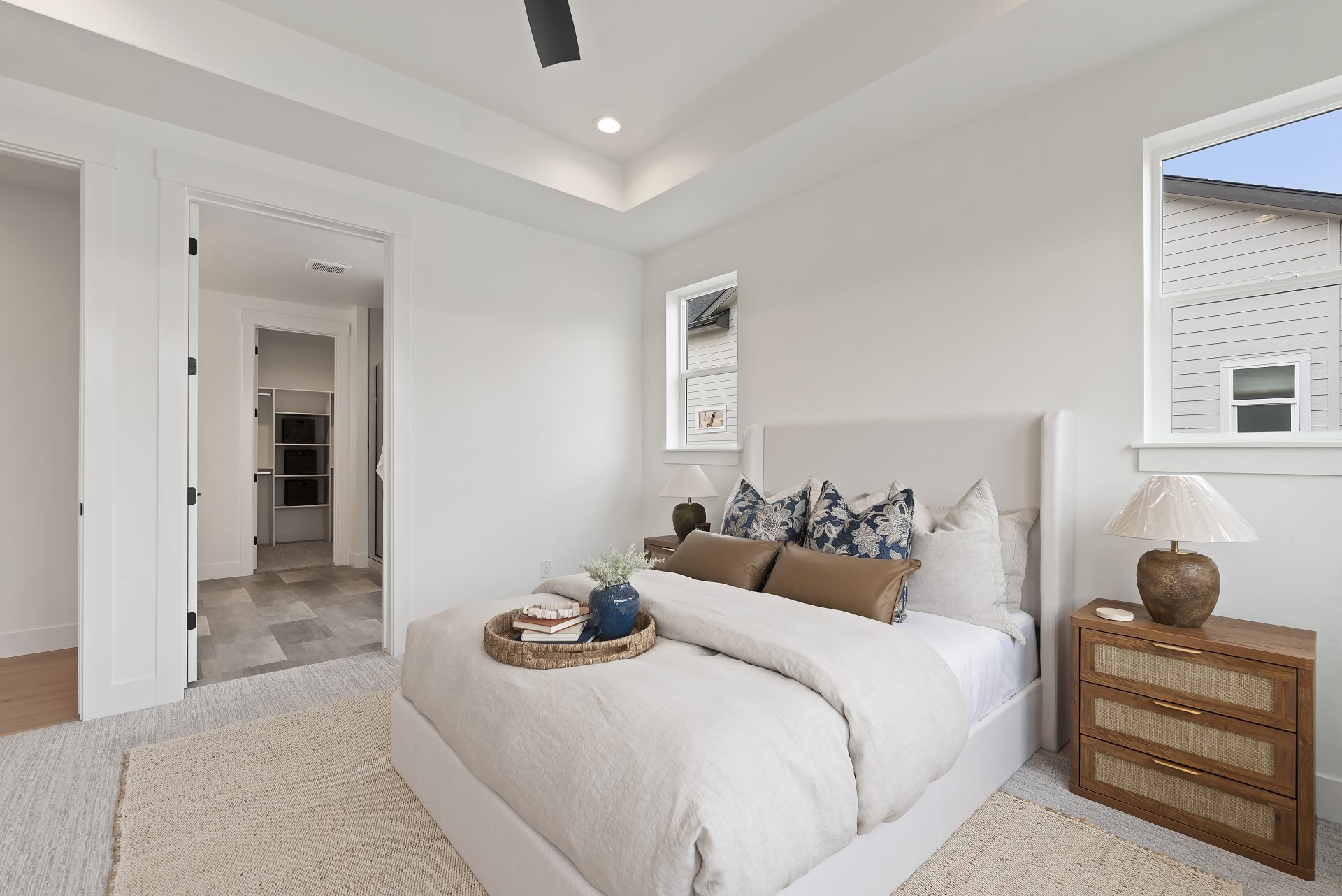 A staged bedroom with gray carpets, light color walls, and black ceiling fan and LED can lighting.