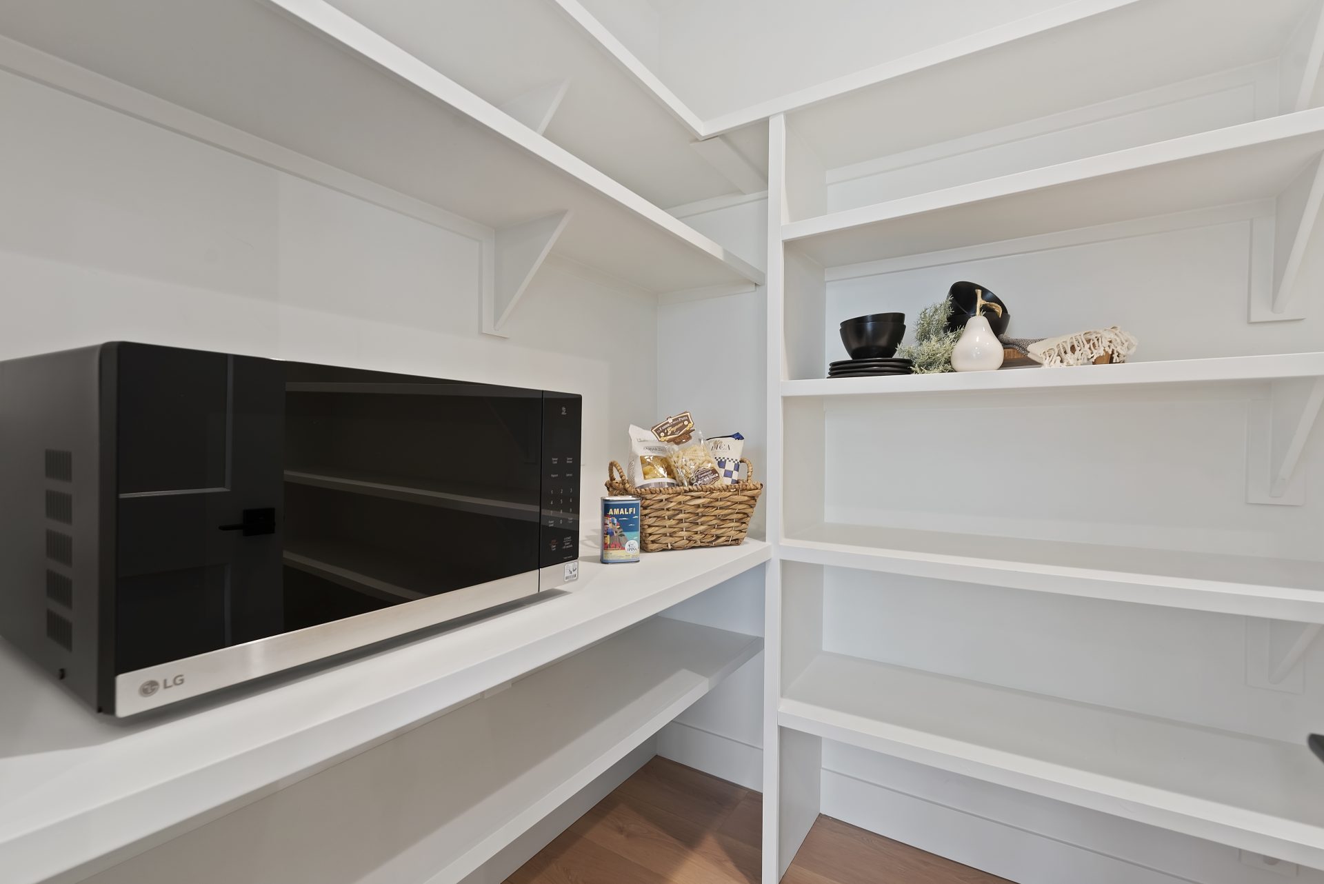 A walk in panty with lots of shelving and a microwave.