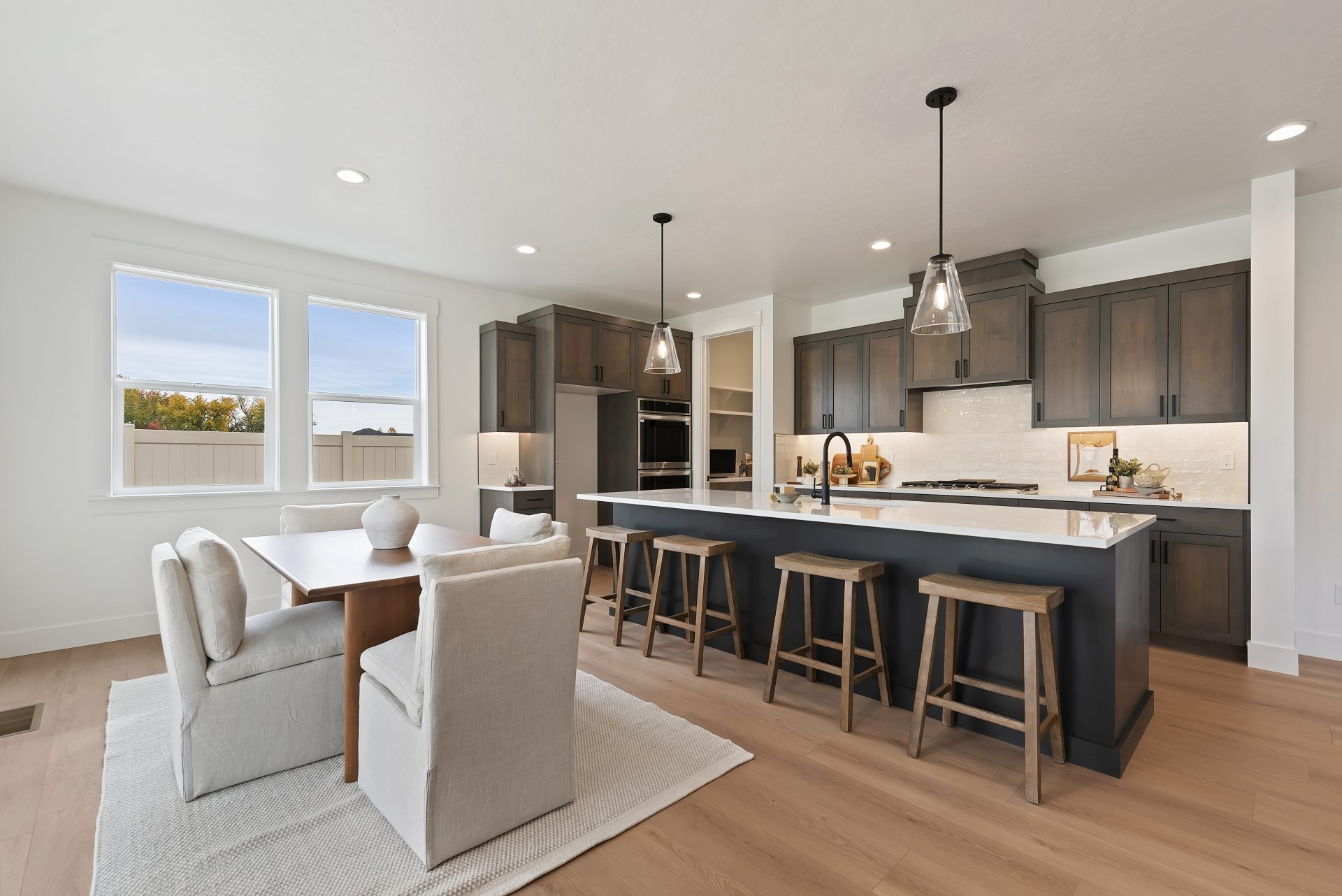 A staged dining area with a table and 4 chains, a kitchen complete with a kitchen island with four seats,  upper and  lower cabinets and a pantry.