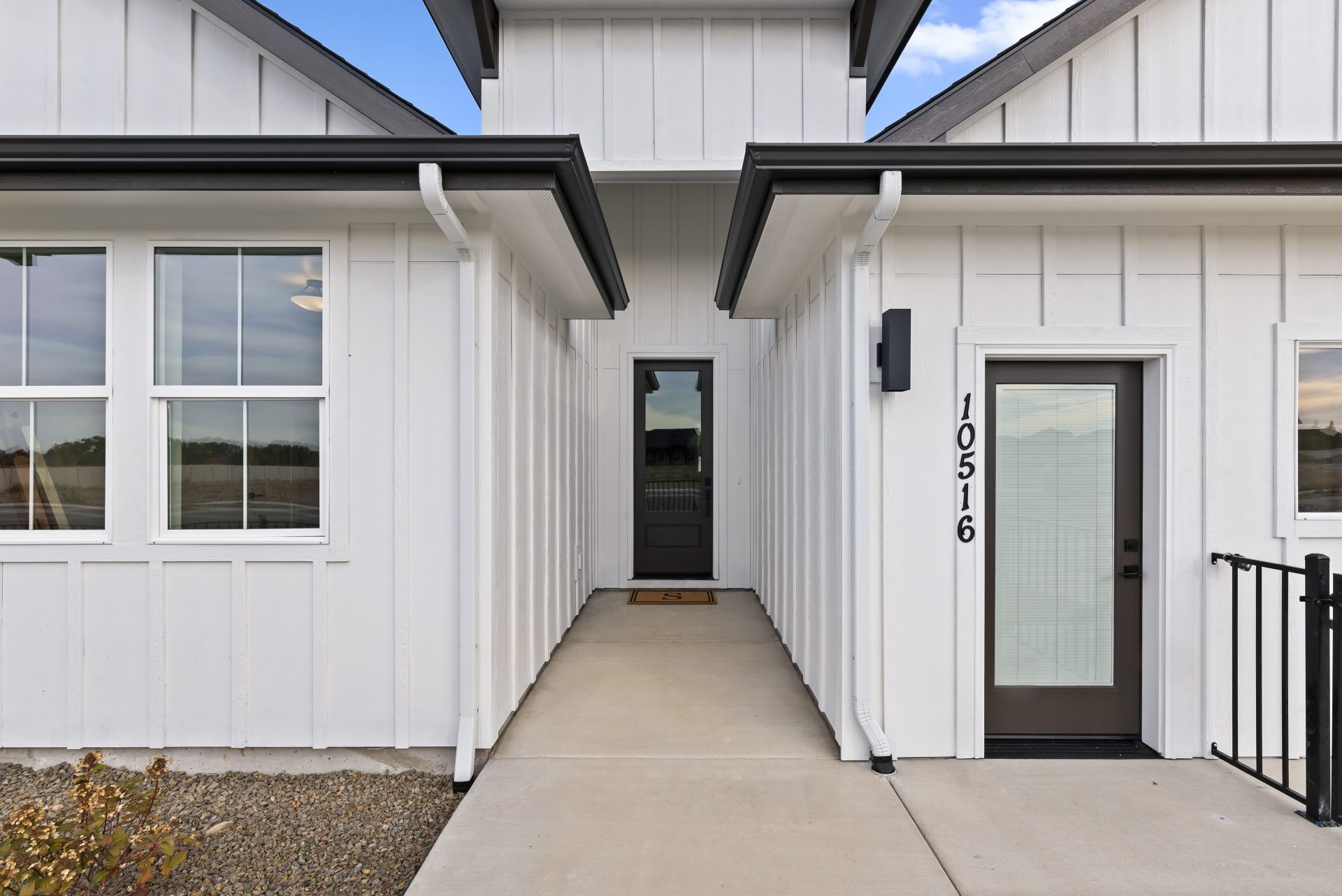 Exterior view of a single story modern home with a light color base and red brick accent, dark roof and dark accents with grass landscaping.