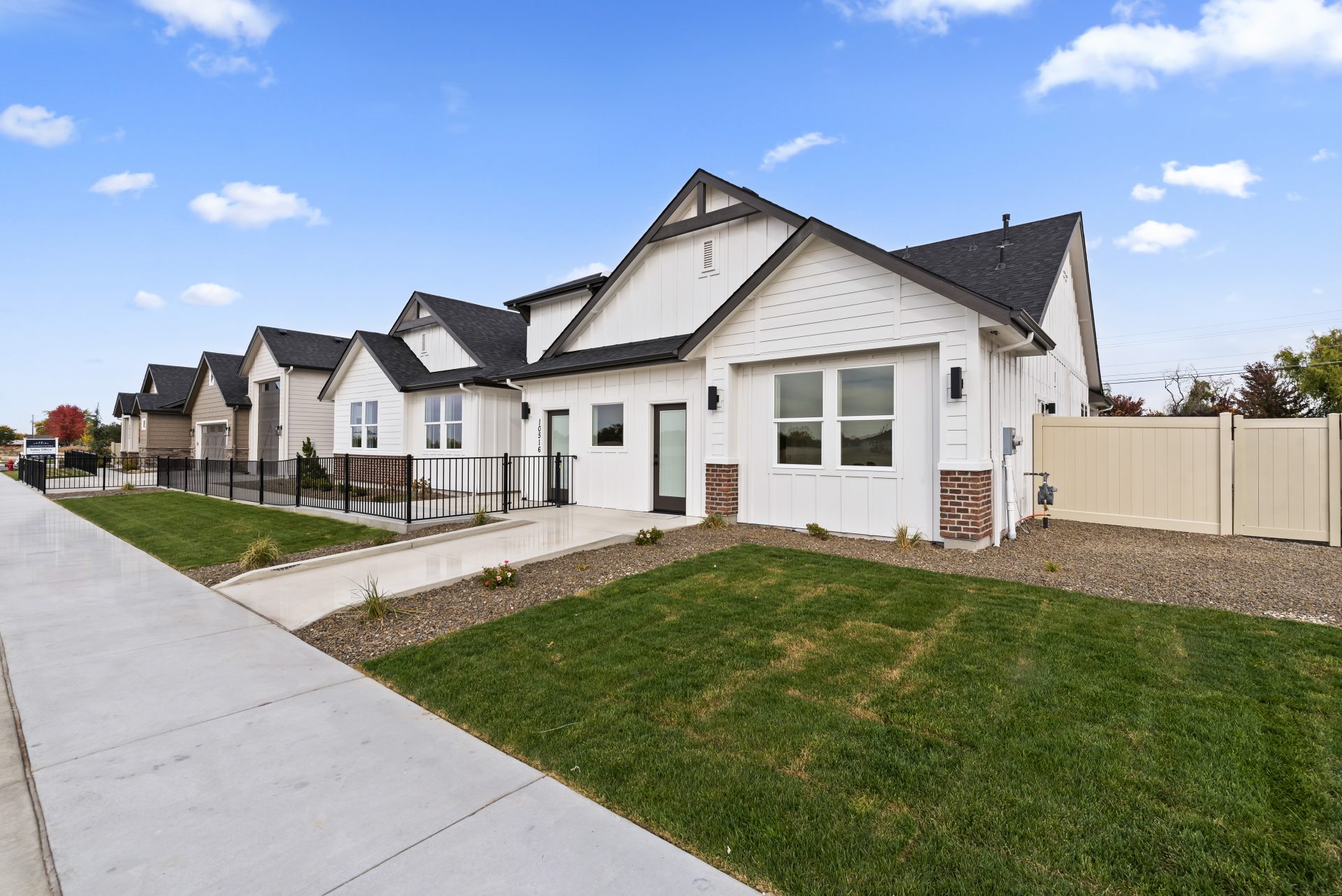 Exterior view of a single story modern home with a light color base and red brick accent, dark roof and dark accents with grass landscaping.