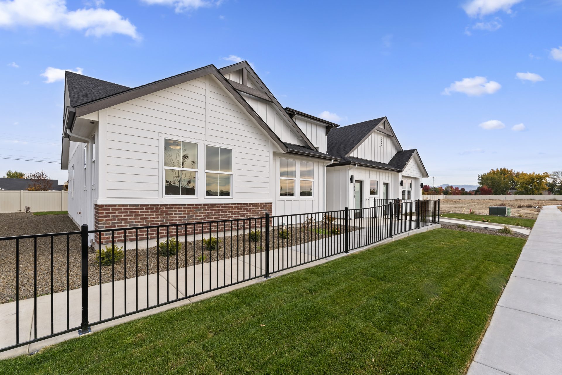 Exterior view of a single story modern home with a light color base and red brick accent, dark roof and dark accents with grass landscaping.
