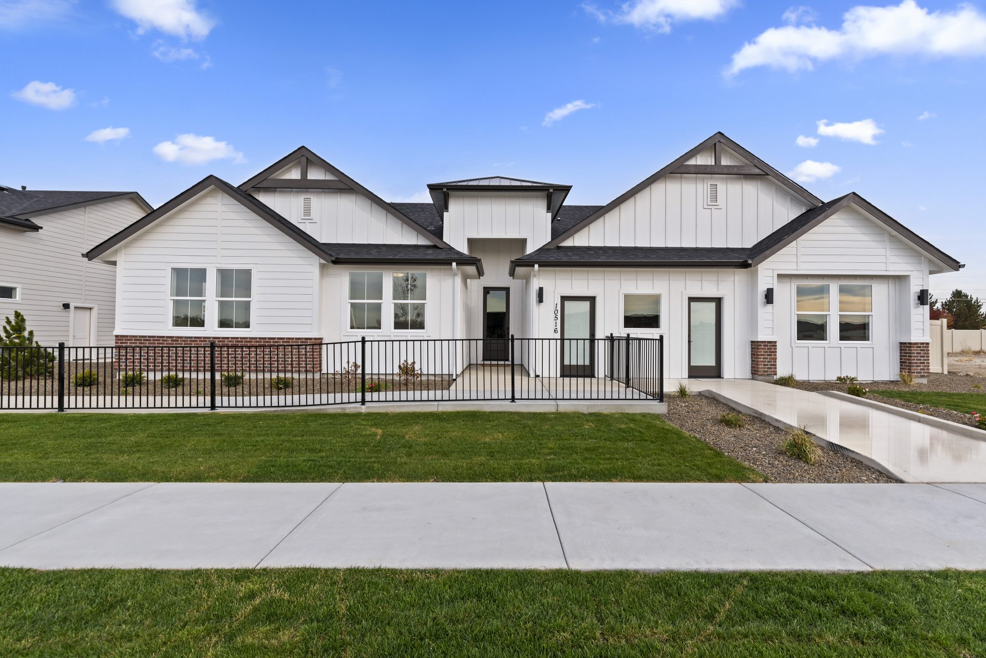 Exterior view of a single story modern home with a light color base and red brick accent, dark roof and dark accents with grass landscaping.