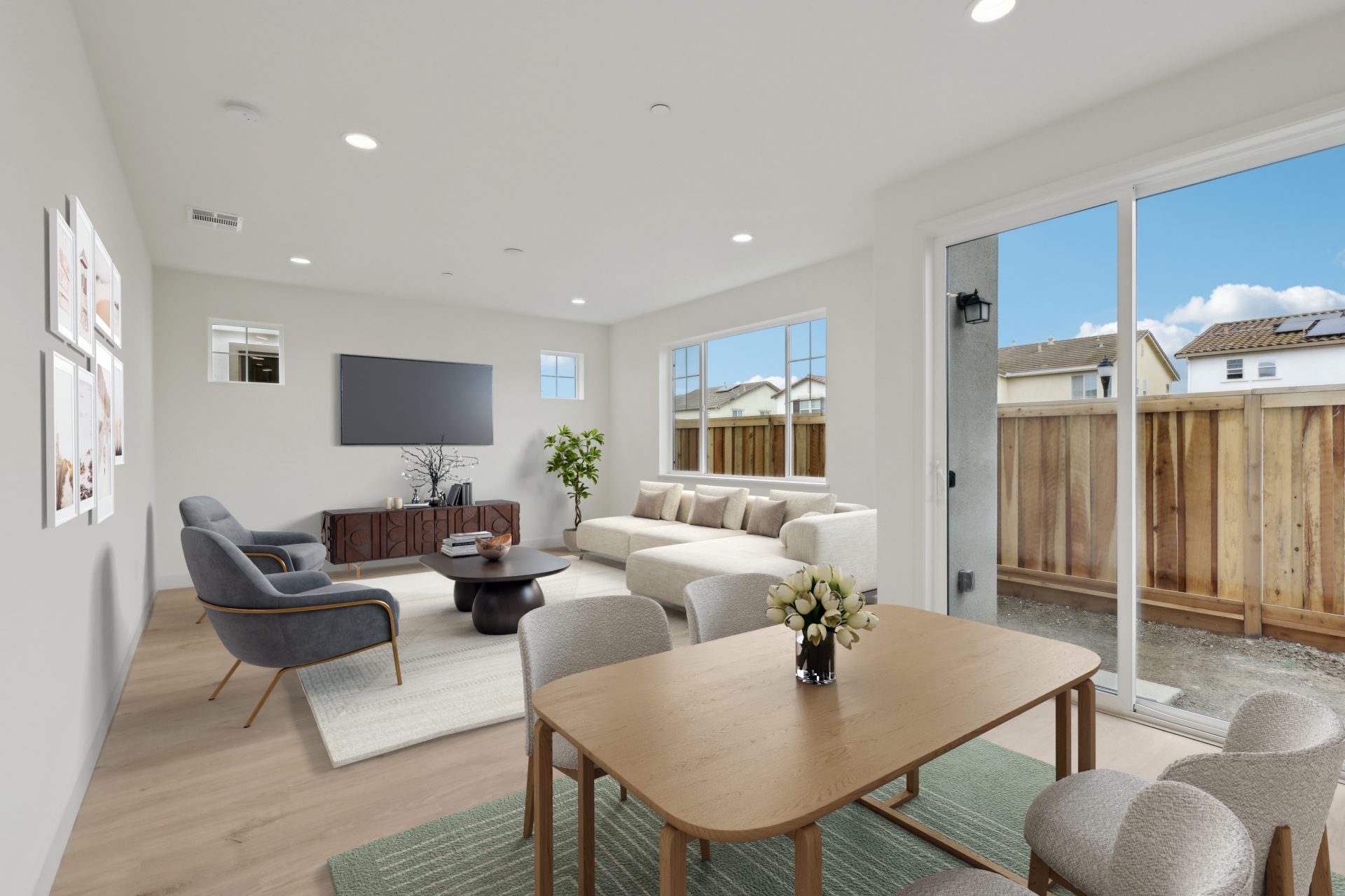 A virtually staged living area with a sectional couch, table and two lounge chairs. Three windows are behind the couch, the dining and kitchen area are seen in the distance with a sliding glass door off the dining and kitchen area.
