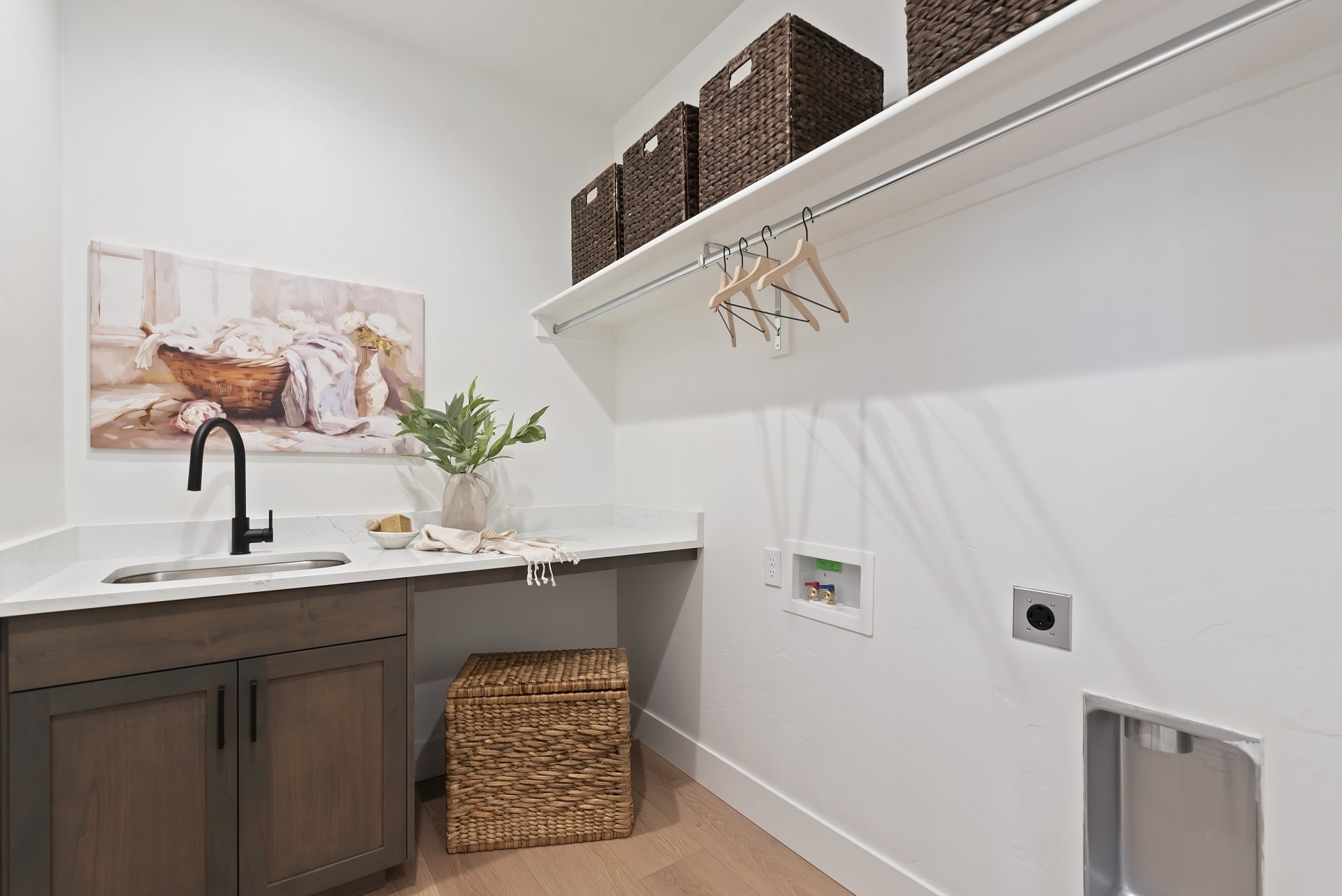 A laundry room with a sink and counterspace with a shelf located along the right wall.