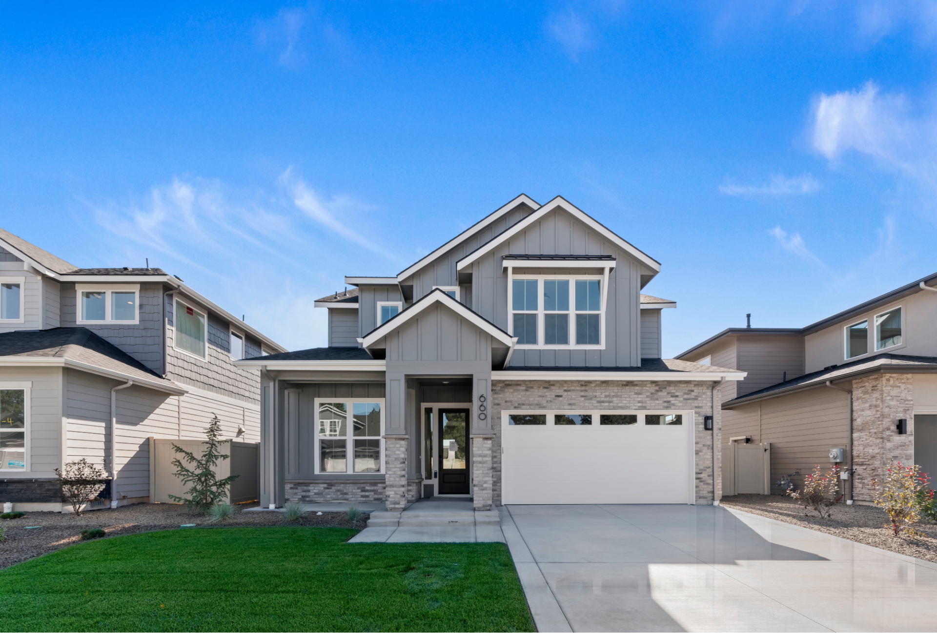 Two-story home with mixed siding, stone accents, two-car garage, and landscaped front yard.