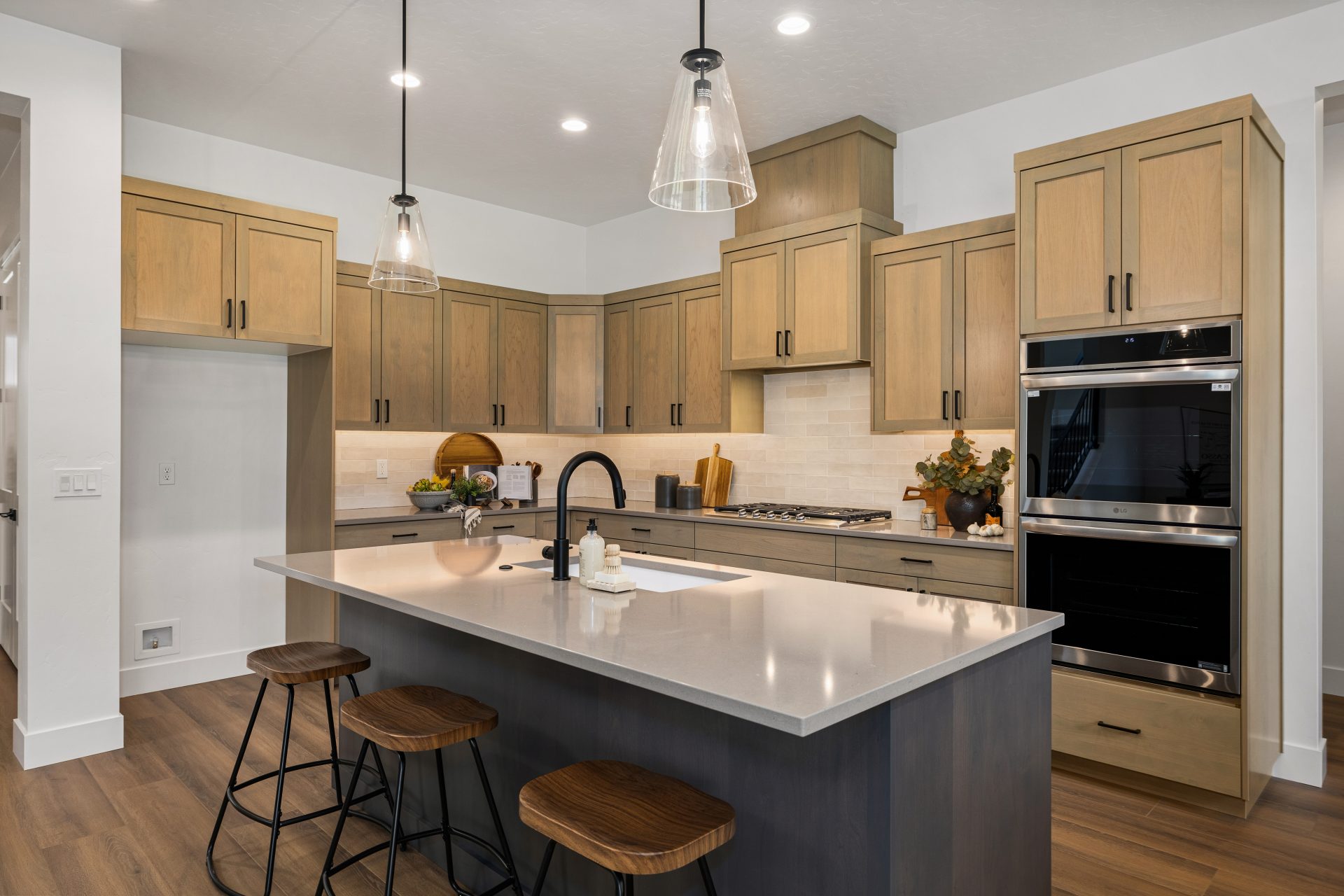 Modern kitchen with wooden cabinetry, double-oven, pendant light fixtures, and center island