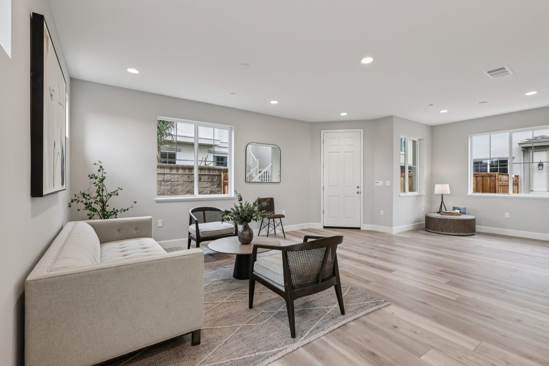 Living room with light gray walls, wood-look flooring, and multiple windows bringing in natural light. Living room with light gray walls, wood-look flooring, and multiple windows bringing in natural light. The space features a neutral sofa, accent chairs,