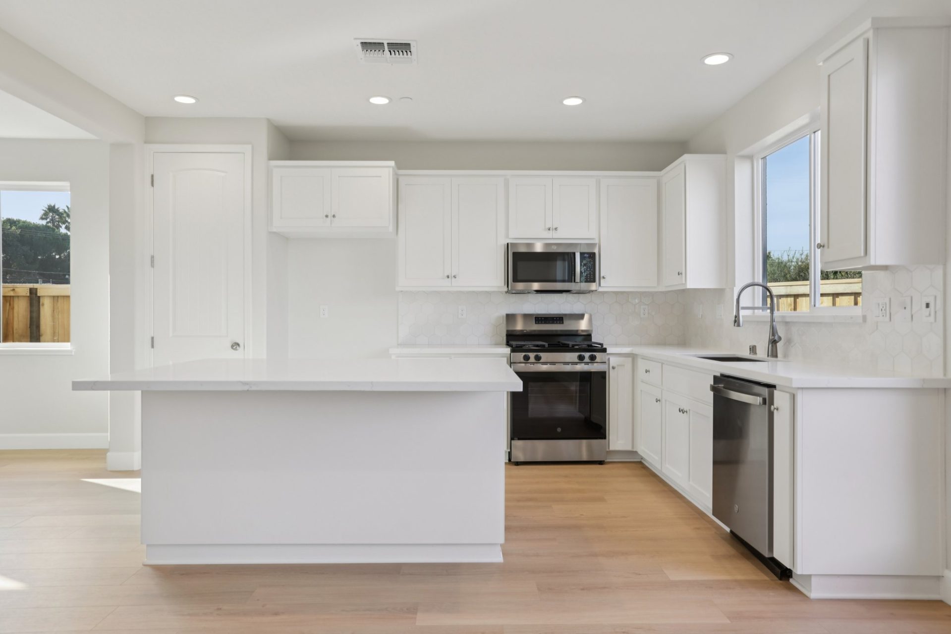 Kitchen with white shaker cabinets, marble-look countertops, and stainless steel appliances. The space features a center island, a gas range with microwave above, and a window above the sink bringing in natural light. Light wood flooring and recessed ligh