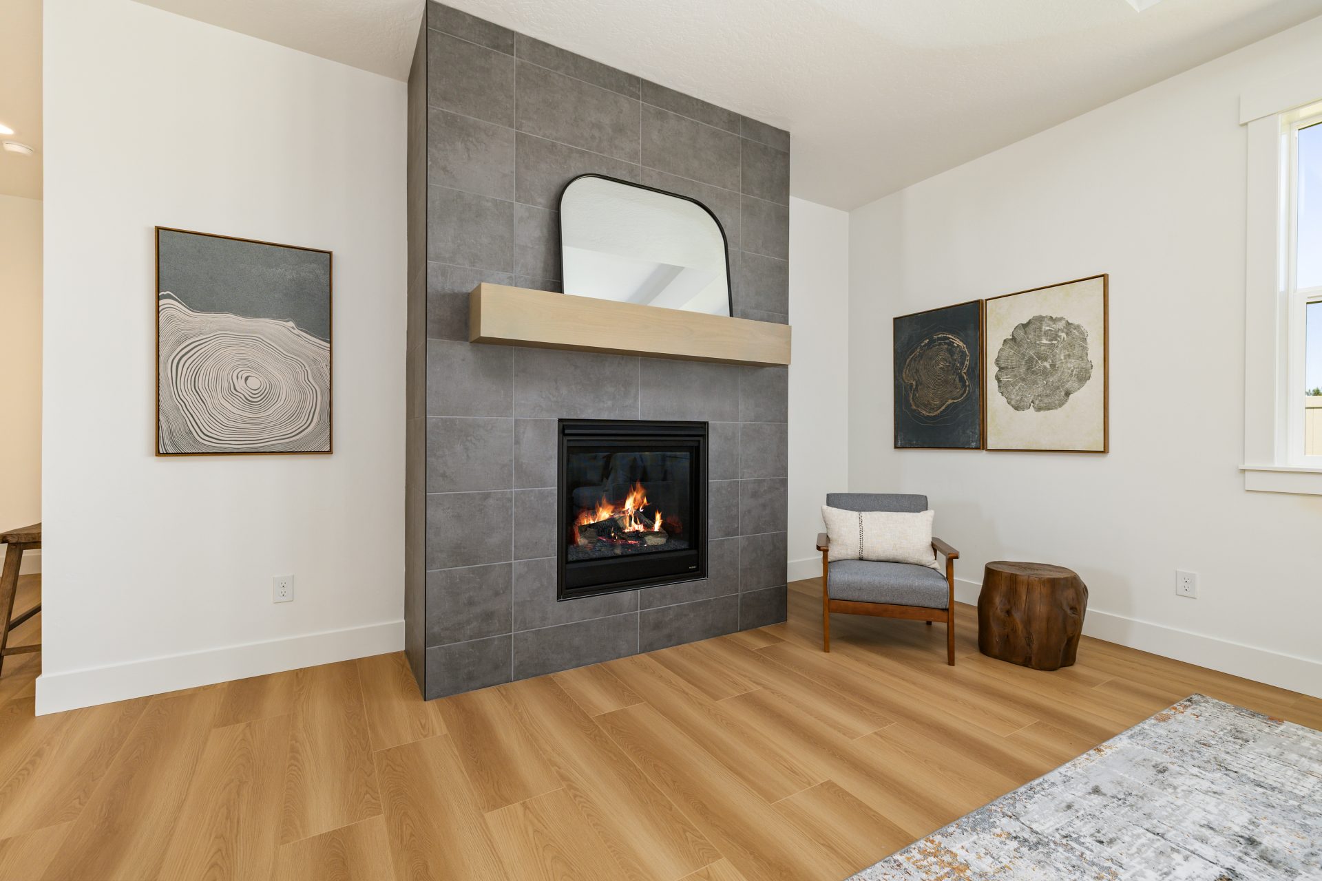 Living room with a tiled fireplace featuring a wood mantel and a mirror above, set against a light wall.Living room with a tiled fireplace featuring a wood mantel and a mirror above, set against a light wall. The space has wood flooring, an accent chair,